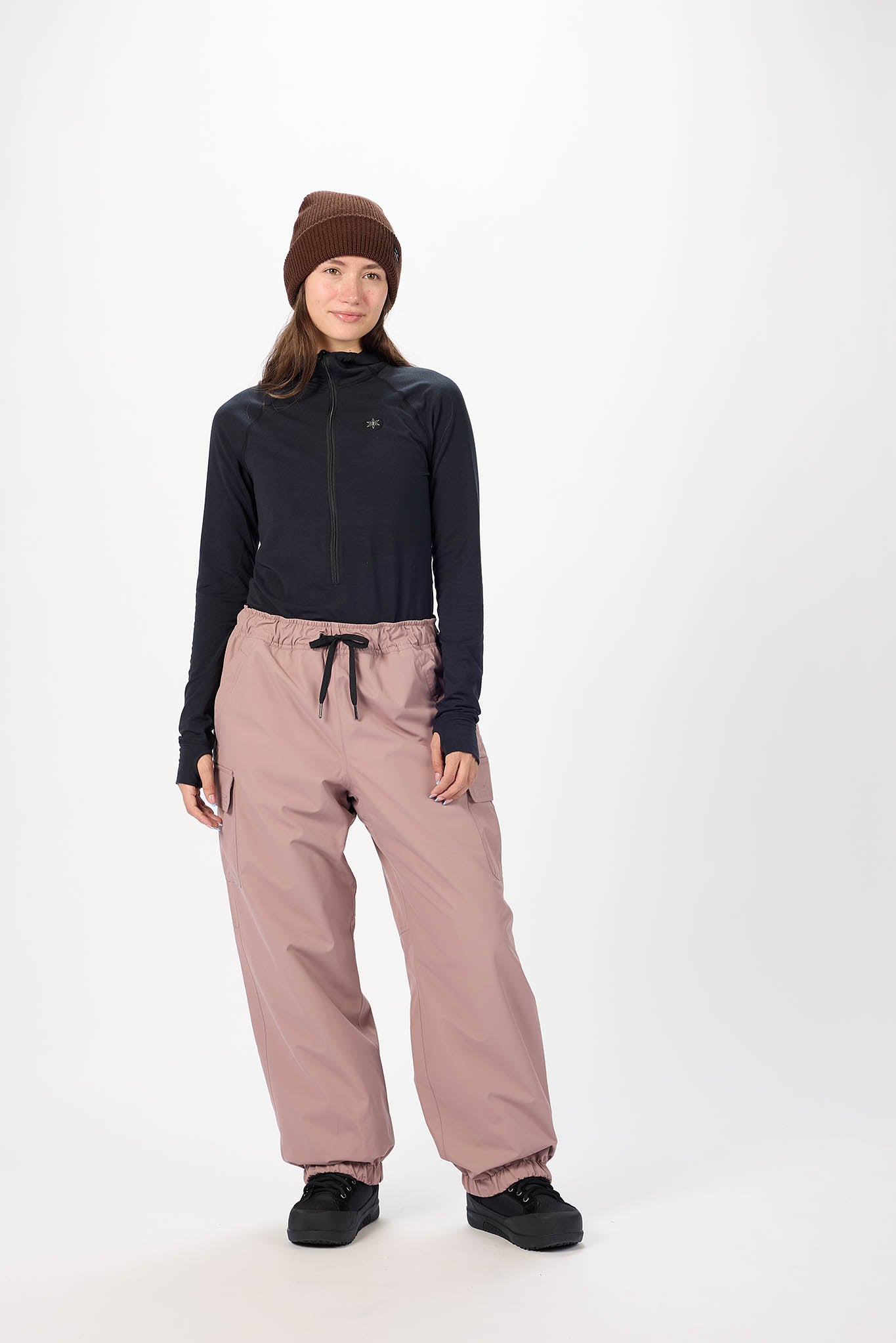 Person wearing a black long-sleeve top and pink pants with a brown beanie on a white background
