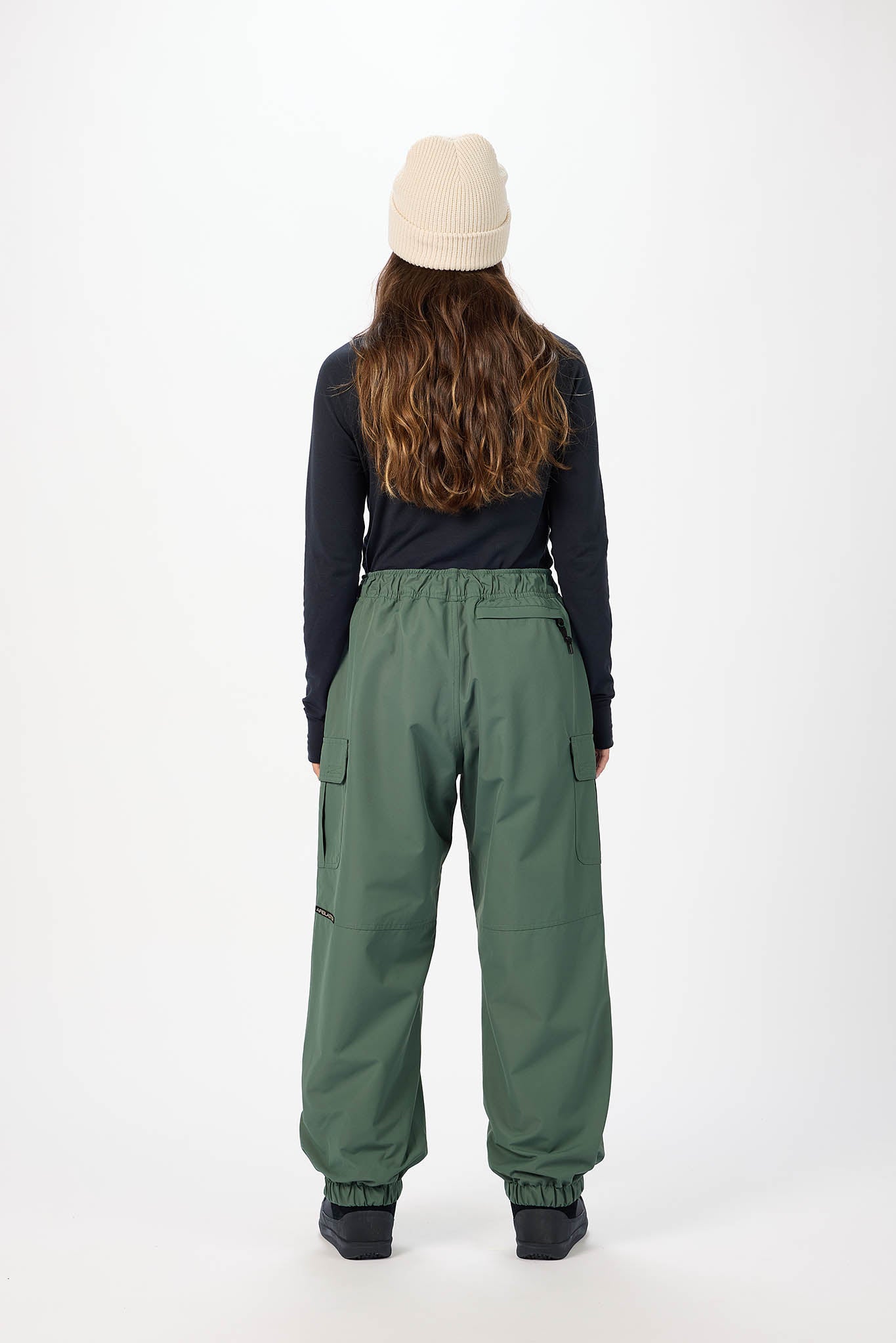 Person wearing green pants and a black jacket with a white background