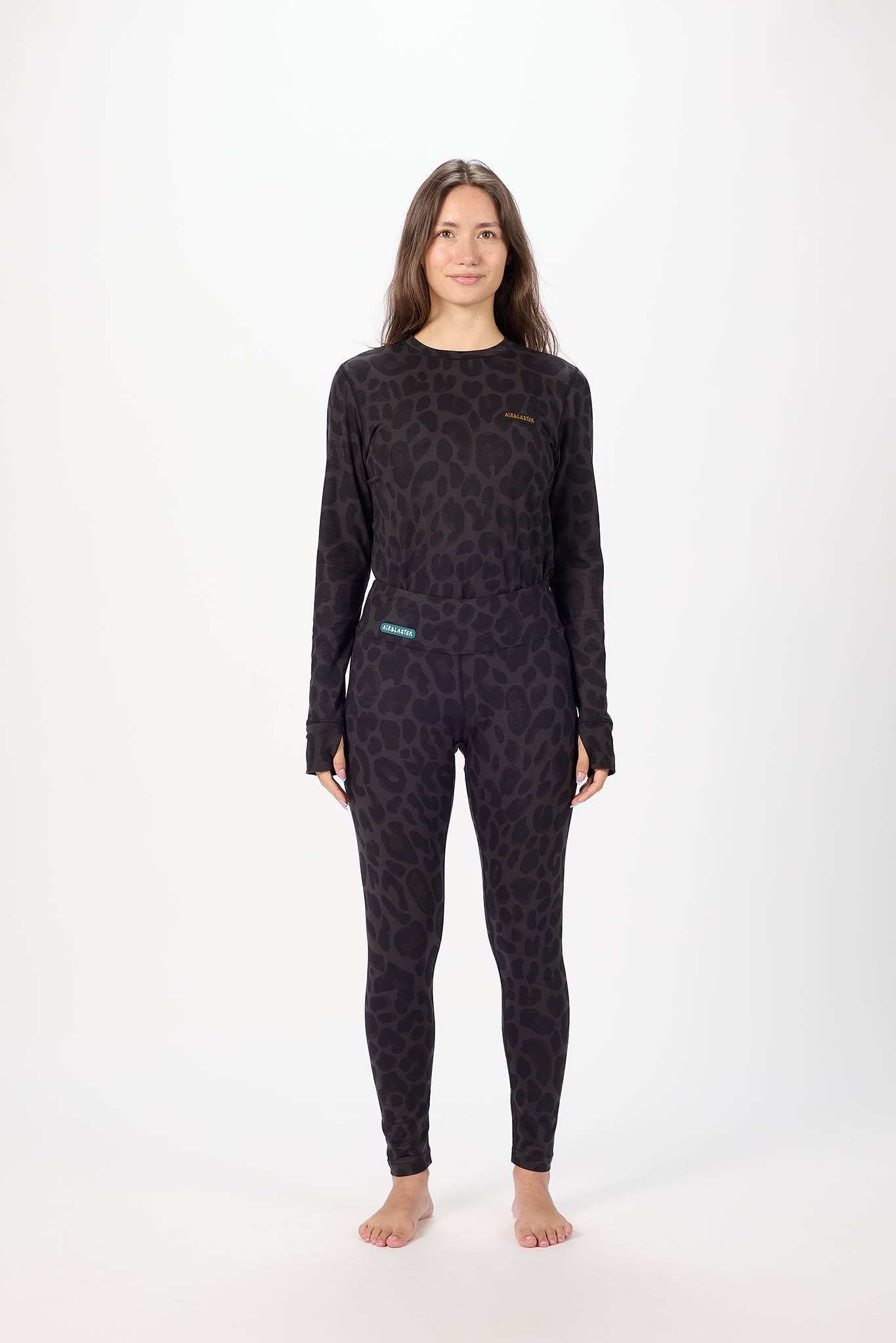 A woman modeling a matching two-piece wetsuit set with a dark leopard print pattern, featuring a long-sleeve top and full-length leggings, against a plain white studio background.