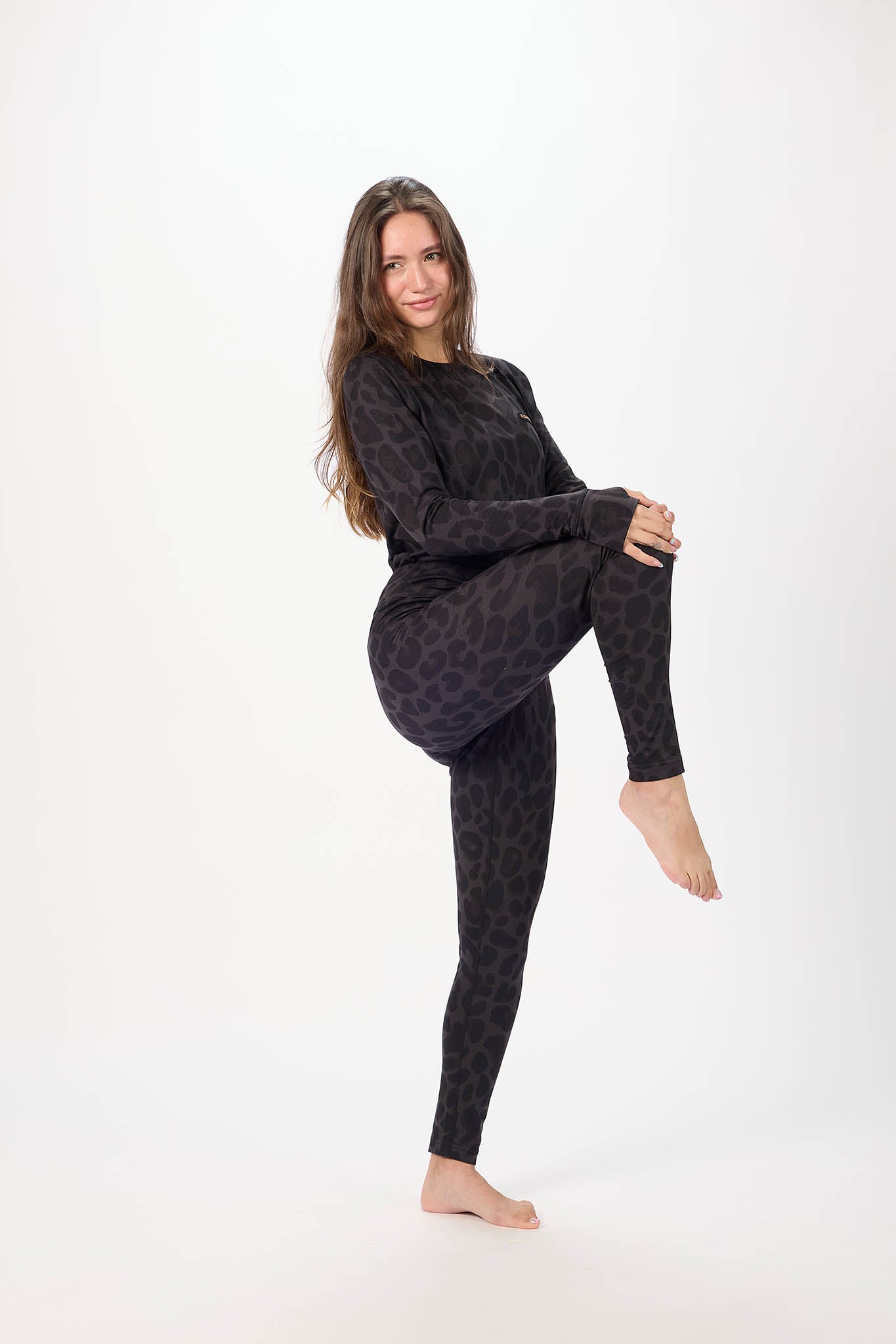A woman posing in a matching black long-sleeve top and high-waisted leggings set with a subtle leopard print pattern, set against a plain white studio background.
