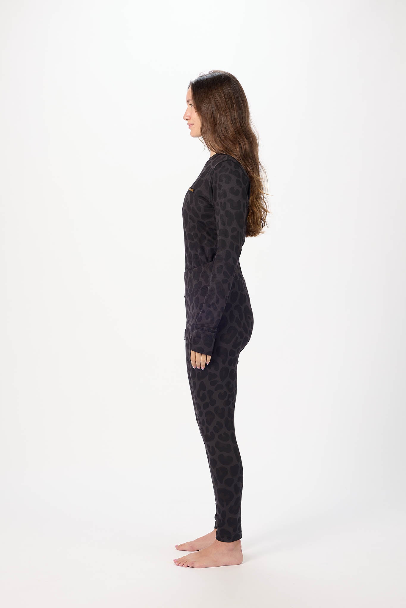 A woman stands in profile wearing a dark patterned long-sleeve top and matching leggings against a plain white studio background.