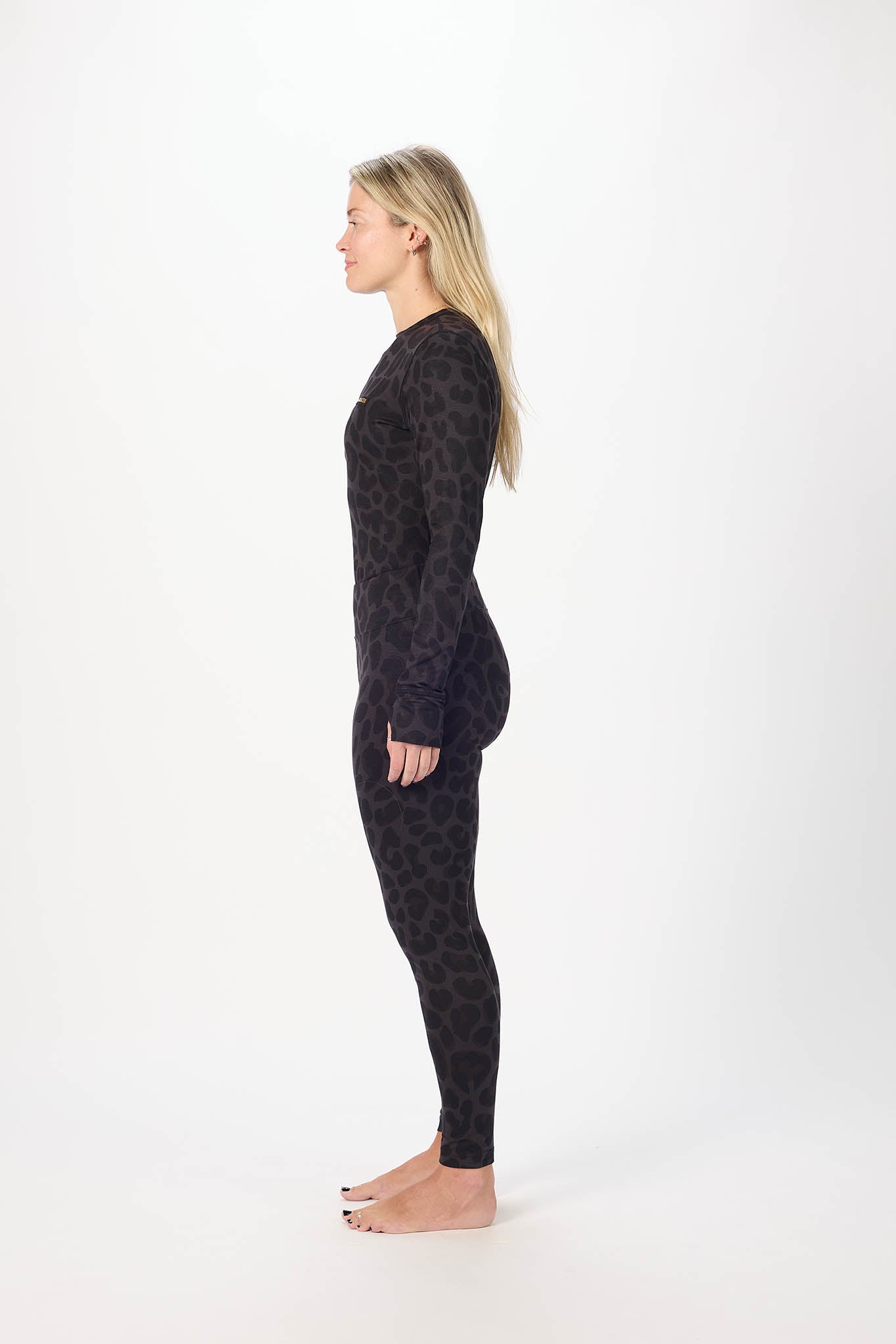 A woman stands in profile against a plain white studio background, wearing a long-sleeve top with leopard print and Leopard leggings.  
