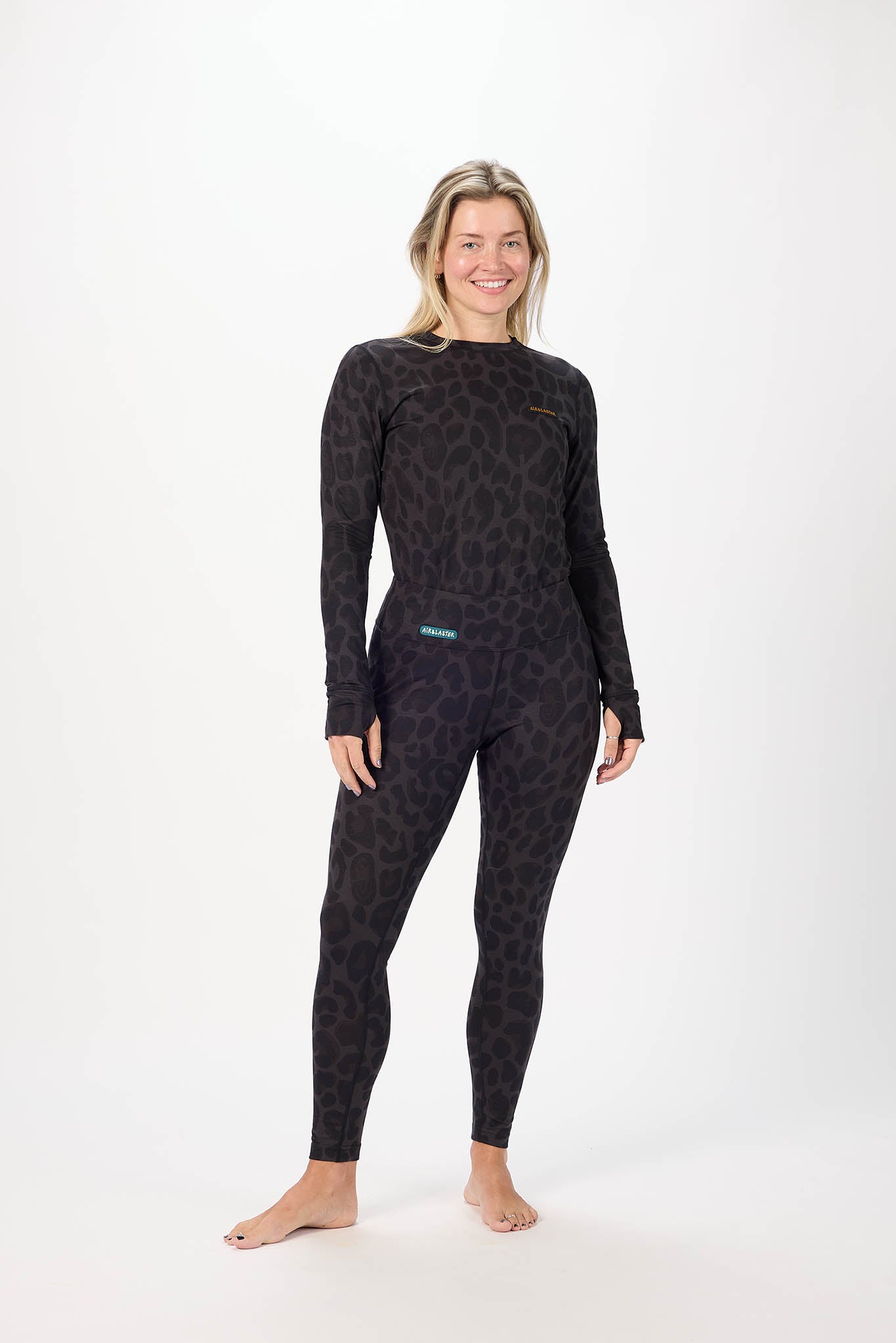 A woman modeling a legwear with a subtle leopard-like pattern, standing against a plain white studio background.