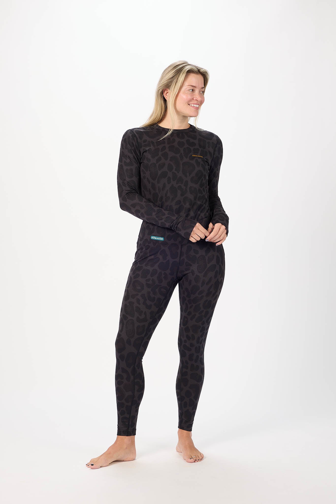 A woman modeling a matching long-sleeve top and full-length leggings set in a dark charcoal gray and black leopard print, standing against a plain white studio background.