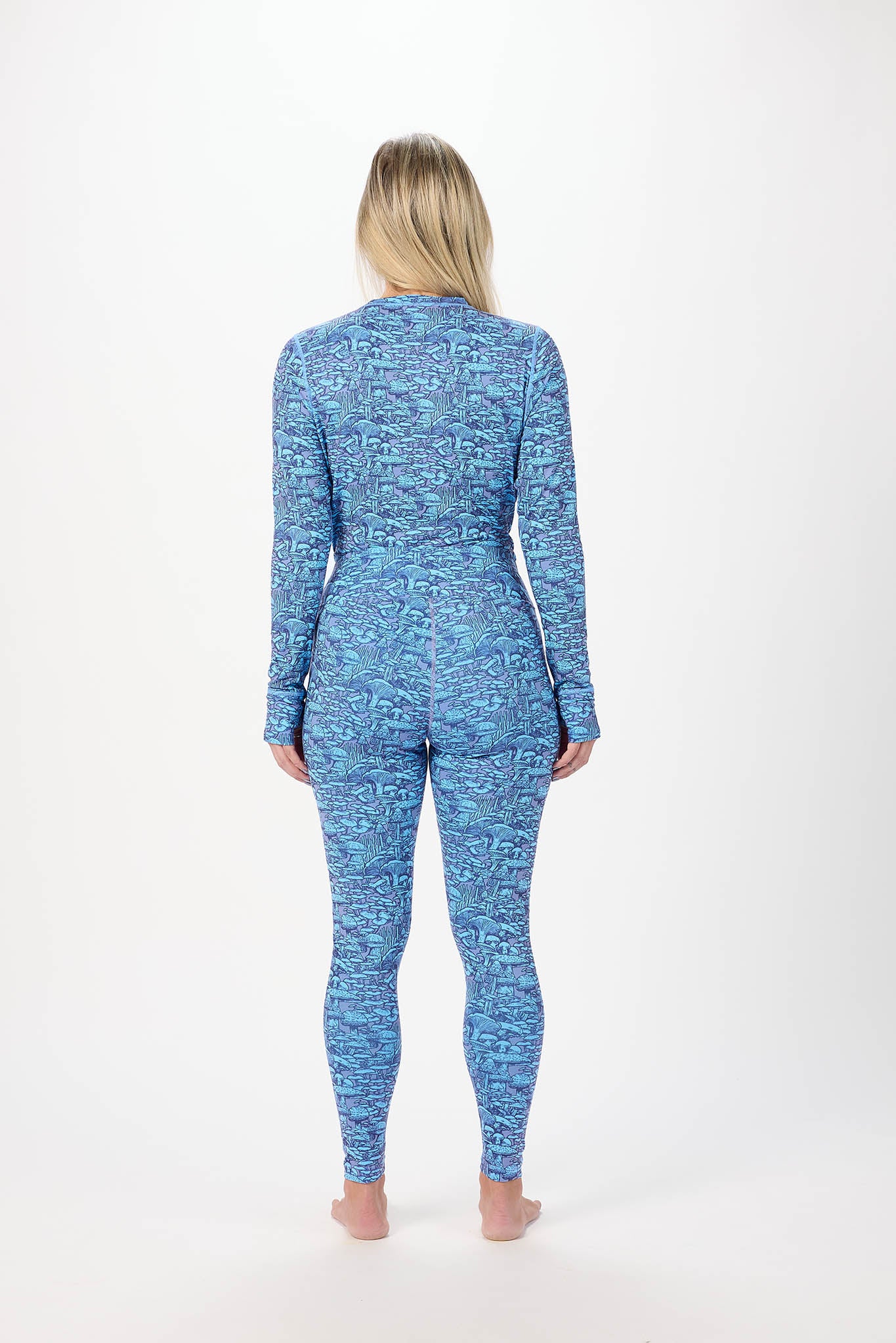 A woman viewed from behind wearing a blue and light blue patterned long-sleeve one-piece jumpsuit against a plain white studio background.