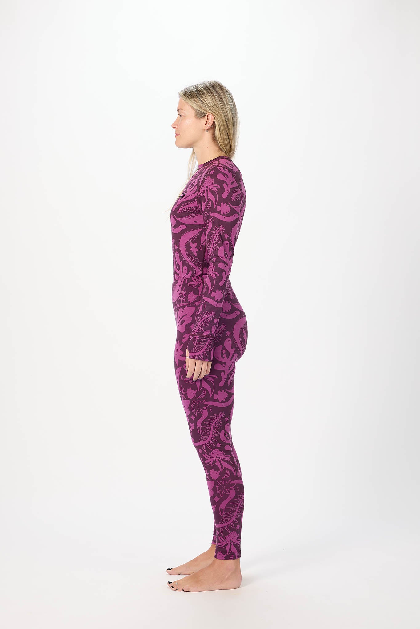 A woman stands in profile wearing a long-sleeve, full-length base layer with an abstract swirling pattern in dark purple and magenta on a light background.