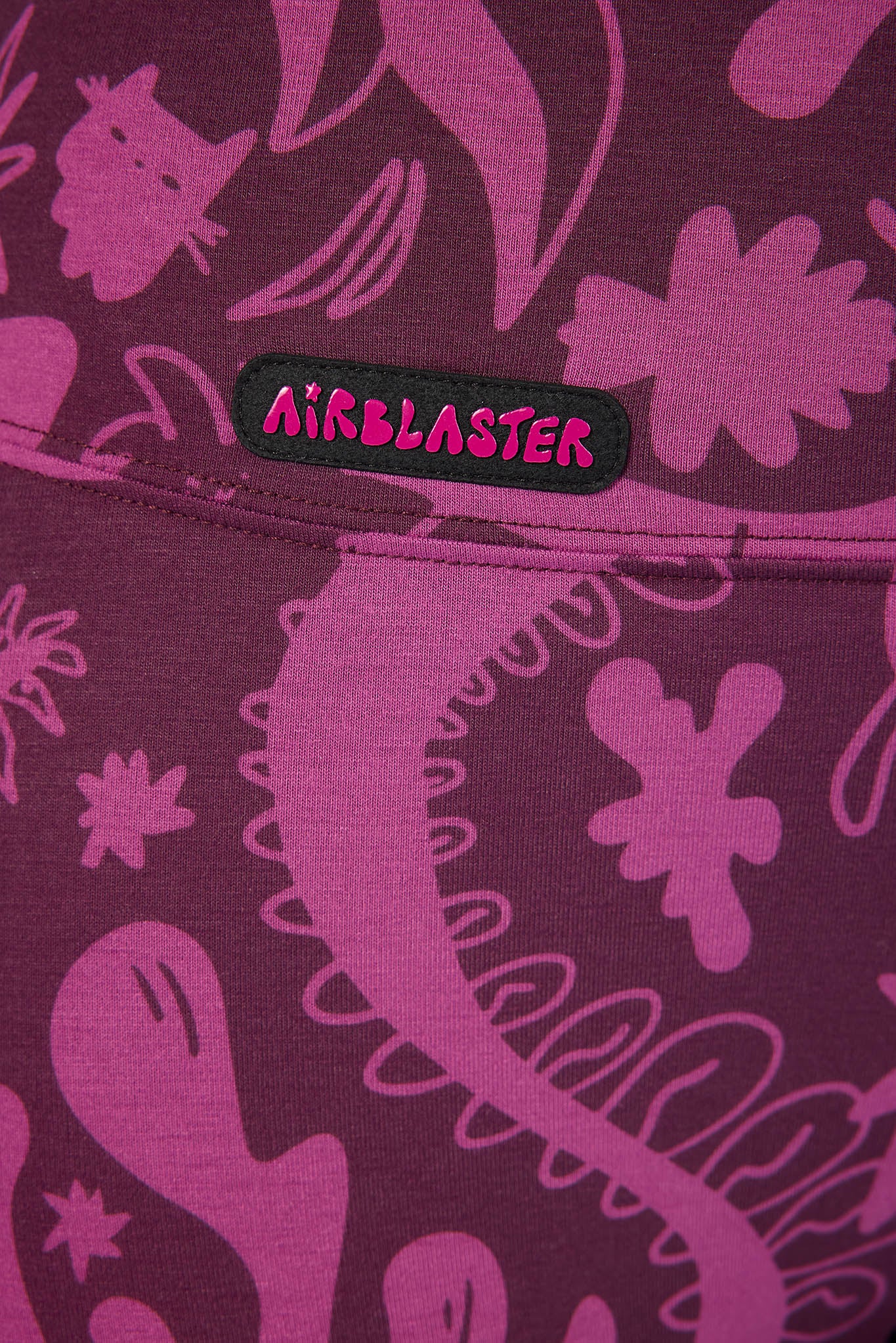 Close-up of a purple and pink patterned garment with a black Airblaster logo patch on the hip.