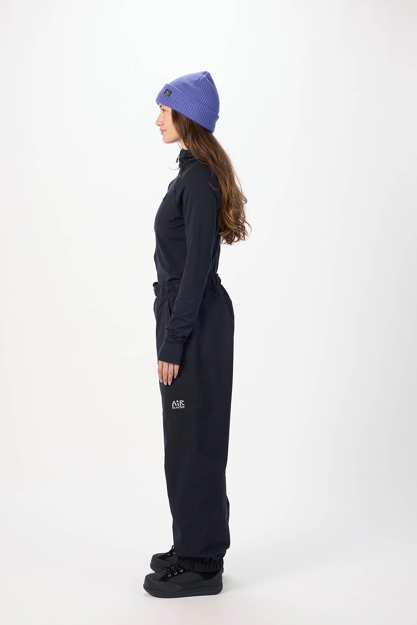 Person wearing a black snowsuit with a purple beanie on a white background