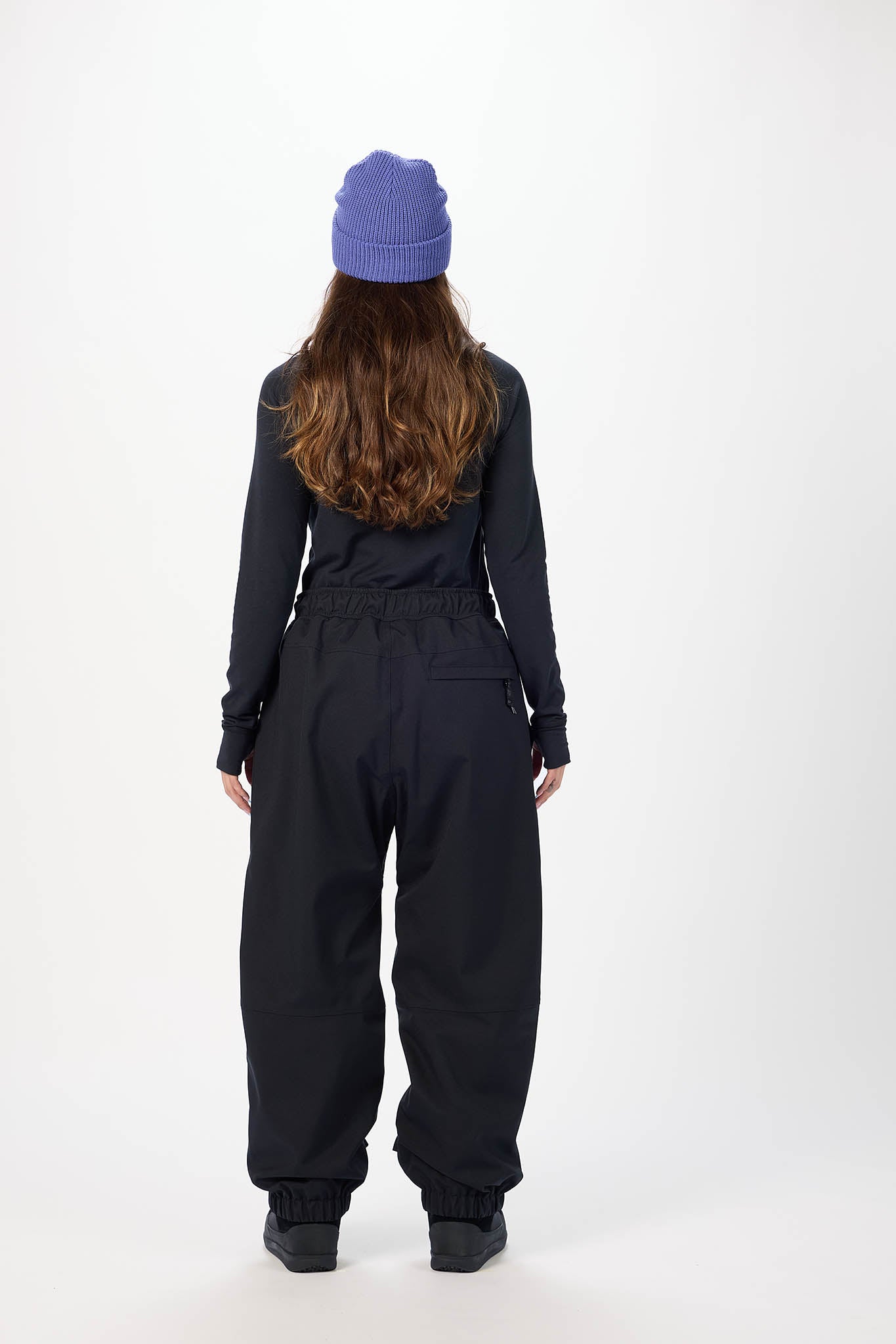 Person wearing a black snowsuit and purple beanie on a white background