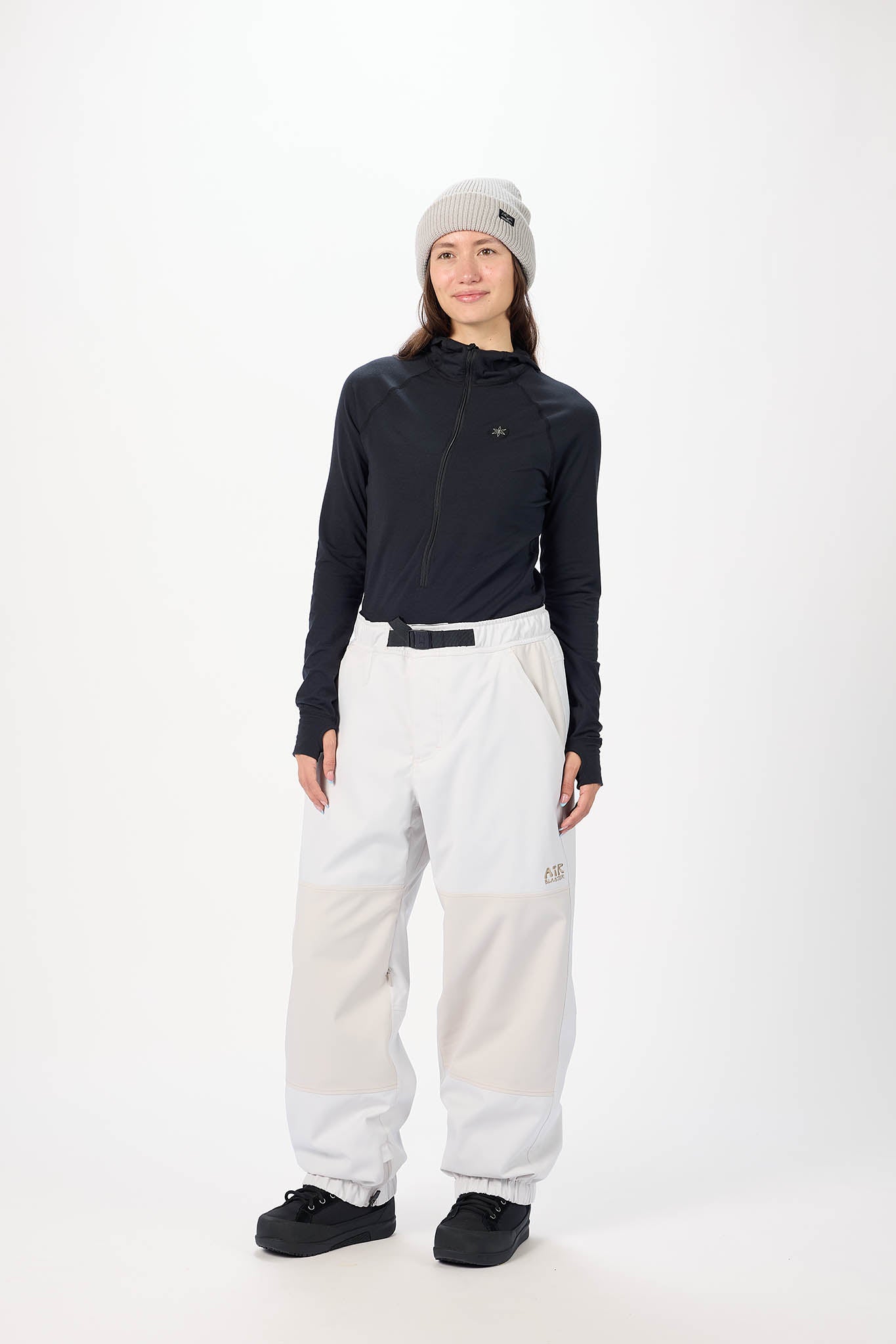 Person wearing a black long-sleeve top, white pants, and a gray beanie on a white background