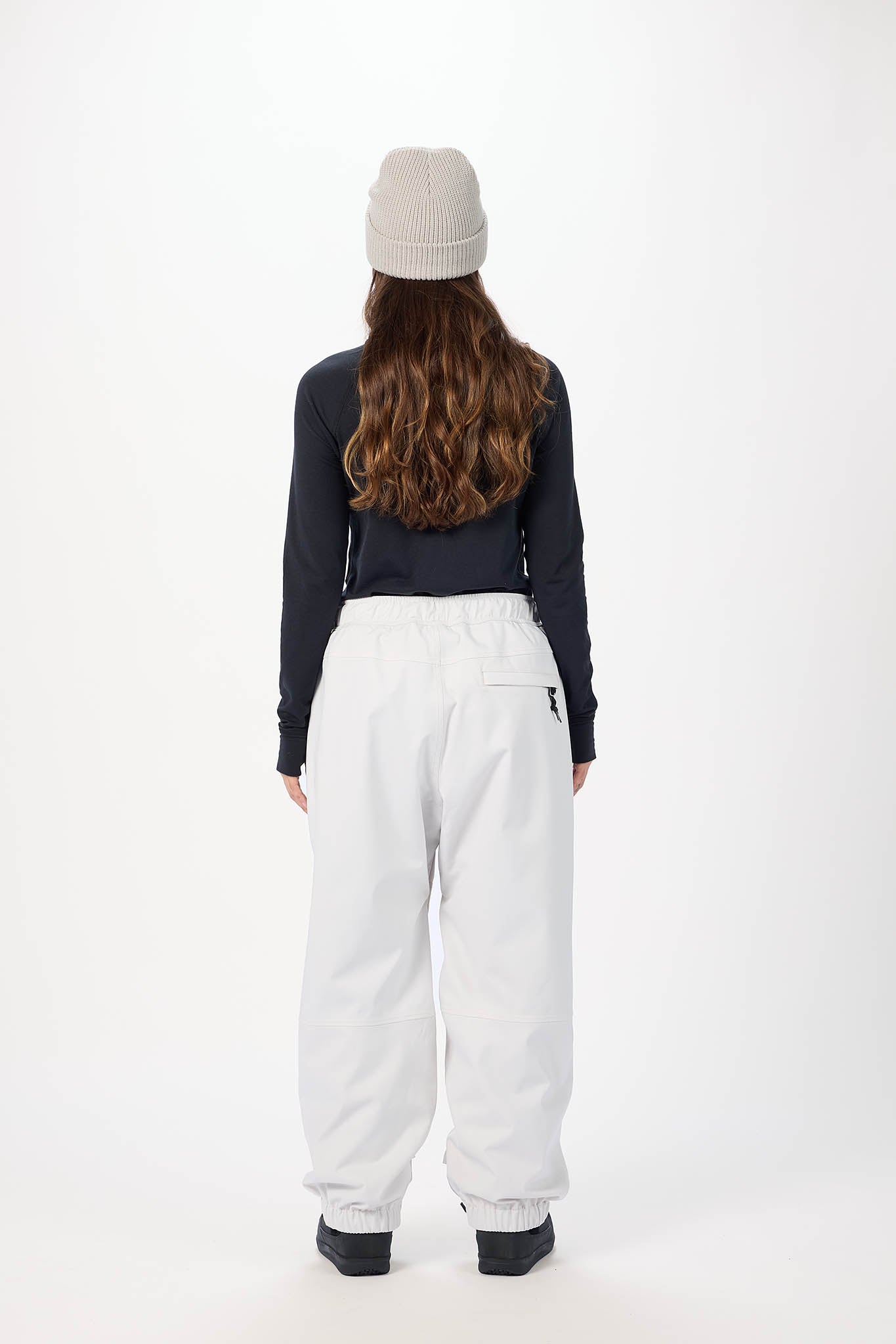 Person wearing a dark long-sleeve top and white pants on a white background