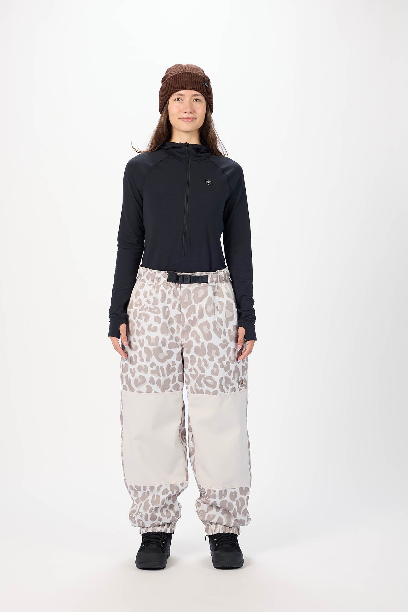 Person wearing a black hoodie, brown beanie, and patterned pants on a white background