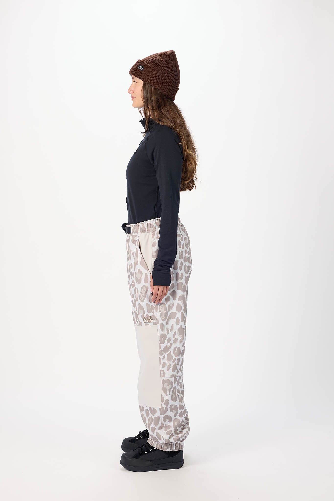 Person wearing a black top, patterned pants, and a brown beanie on a white background