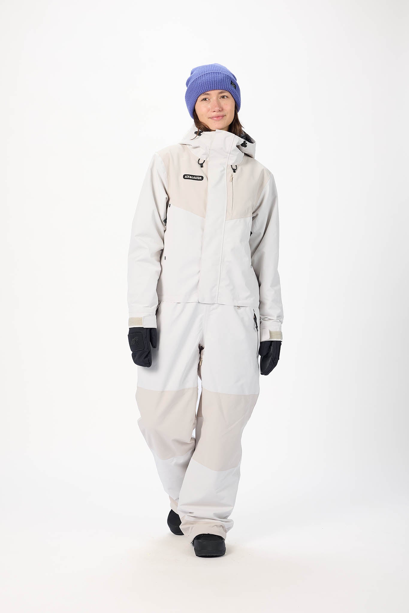 Person wearing a light gray snowsuit with a purple beanie on a white background