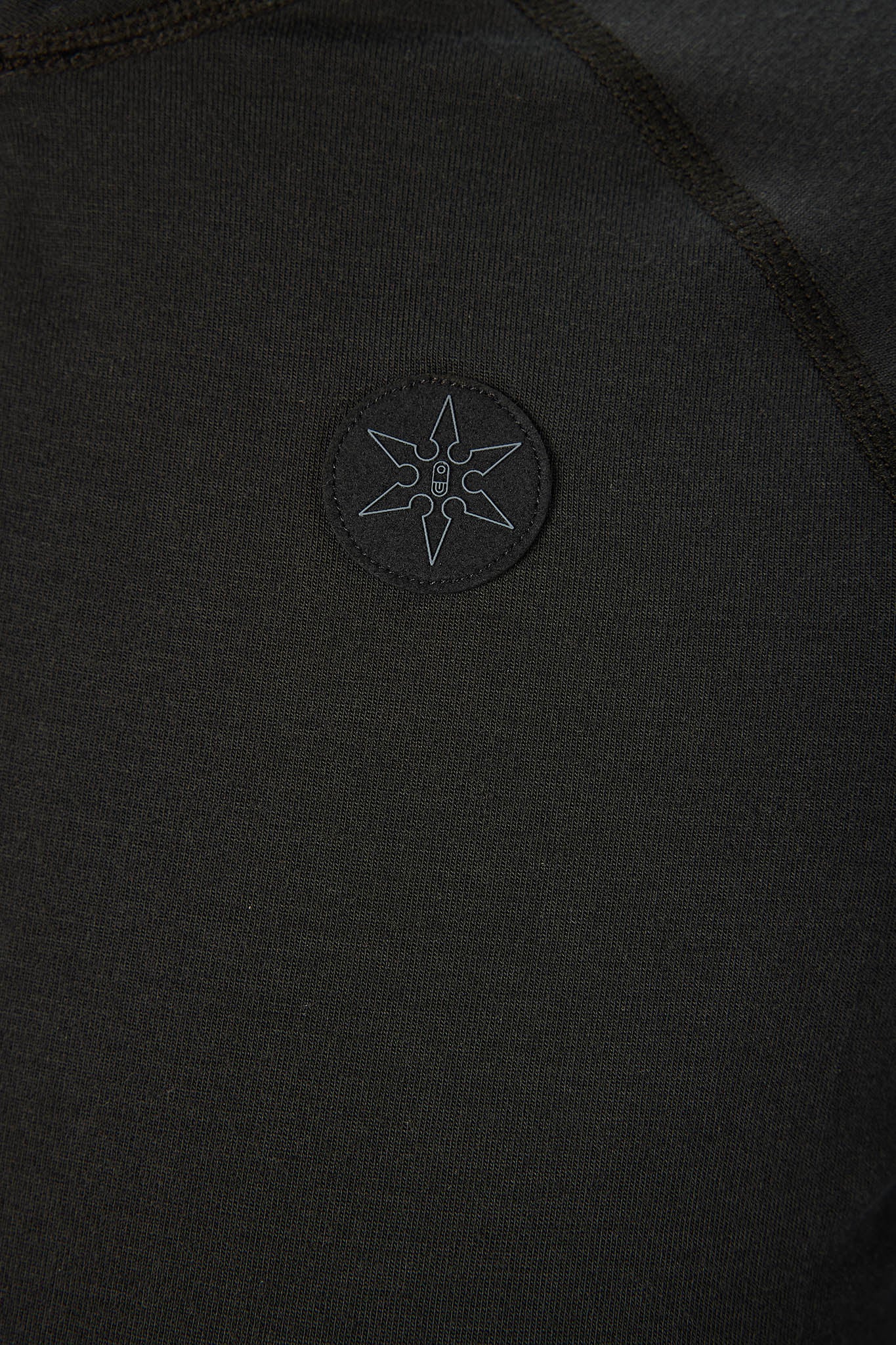 Close-up of a black knit garment featuring a circular embroidered patch with a six-pointed star and a central 'B' logo.