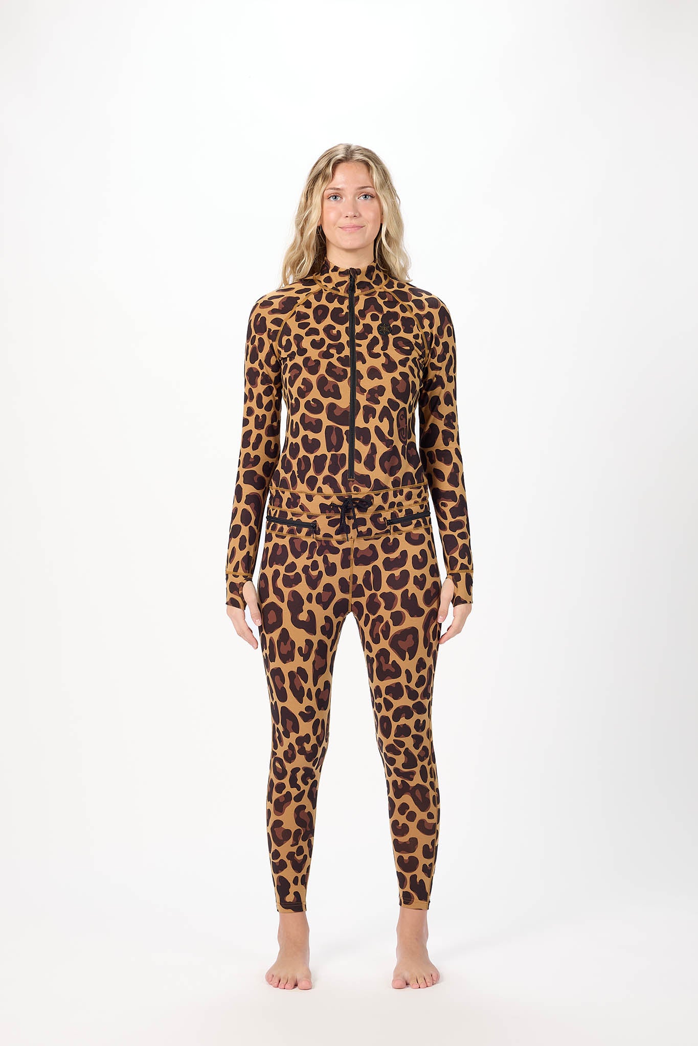 A woman modeling a full-body leopard print zip-up one-piece swimsuit or wetsuit against a plain white studio background.