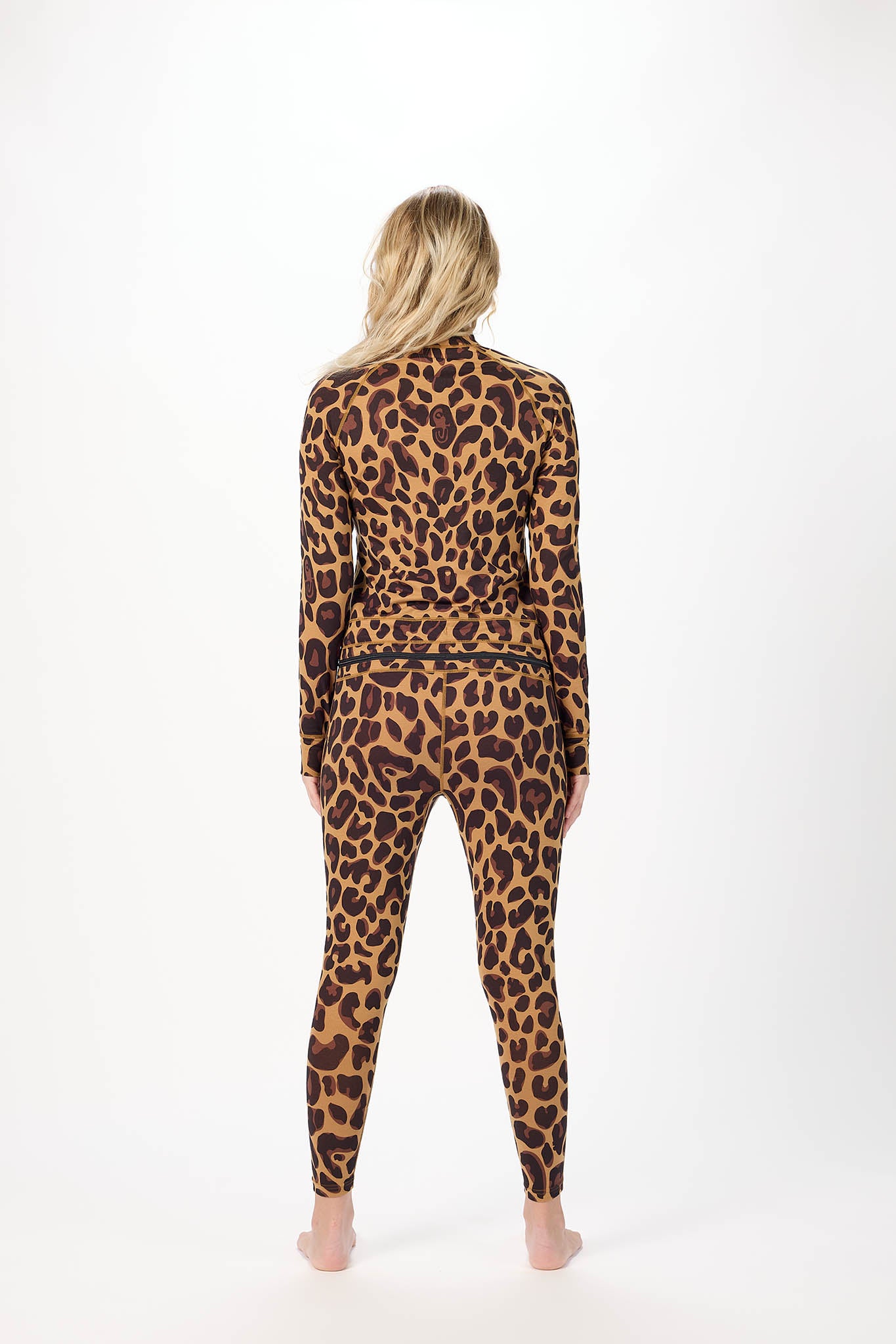 A woman viewed from behind wearing a matching long-sleeve top and leggings set in a brown and black leopard print, standing against a plain white studio background.