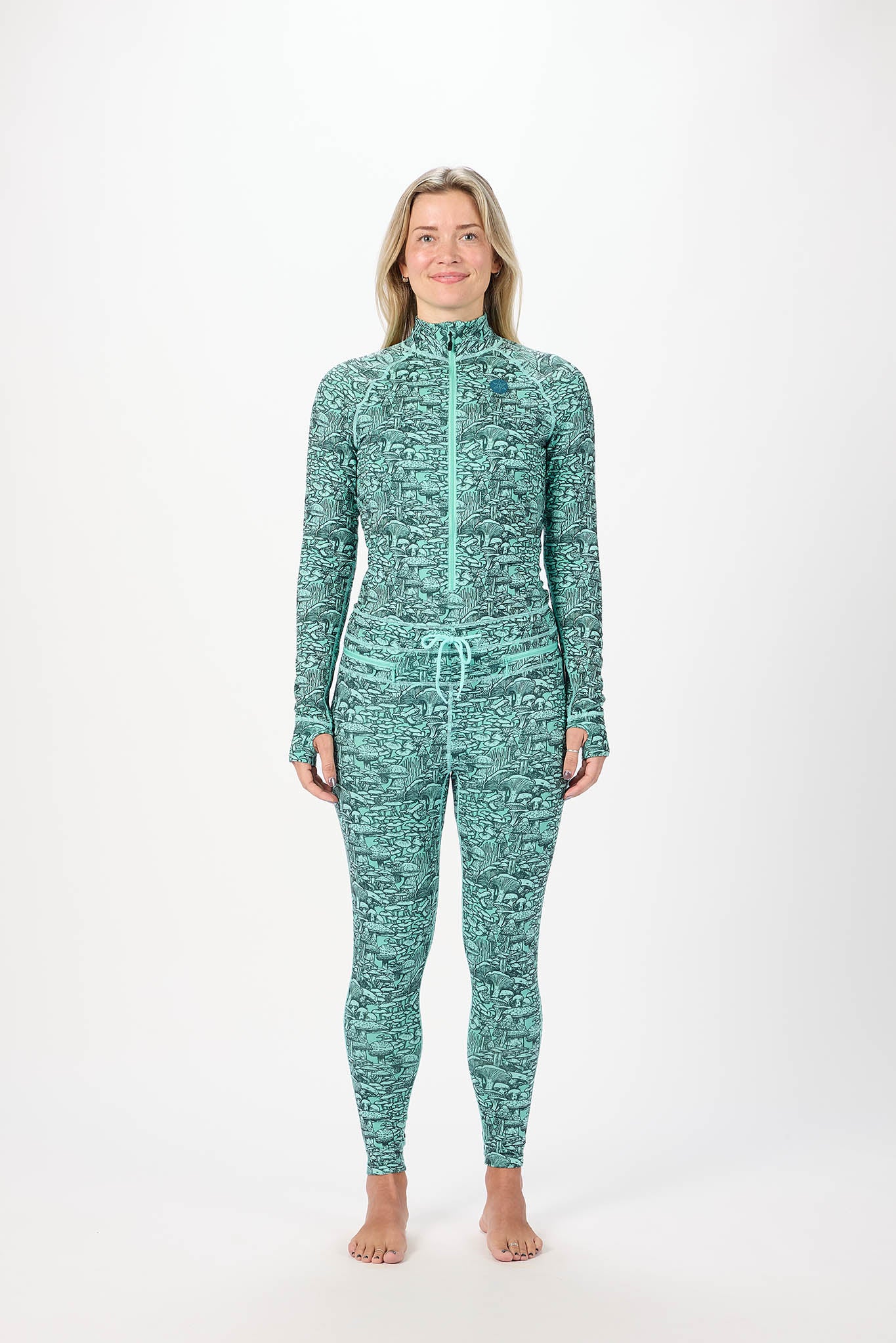 A woman modeling a matching long-sleeve zip-up top and full-length leggings set in a green and white abstract pattern, standing against a plain white studio background.