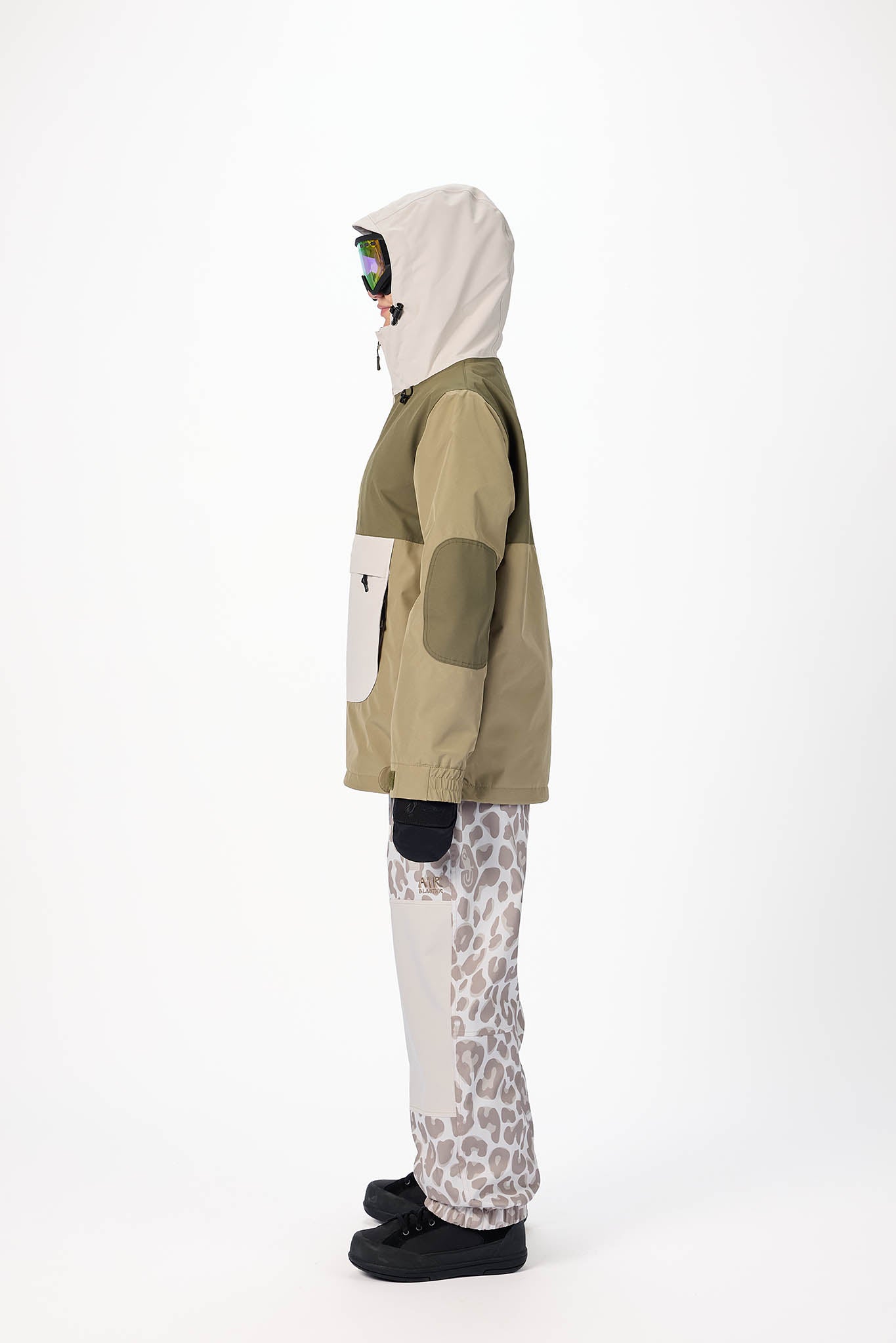 Person wearing a green and beige jacket with a white hood, standing against a white background.