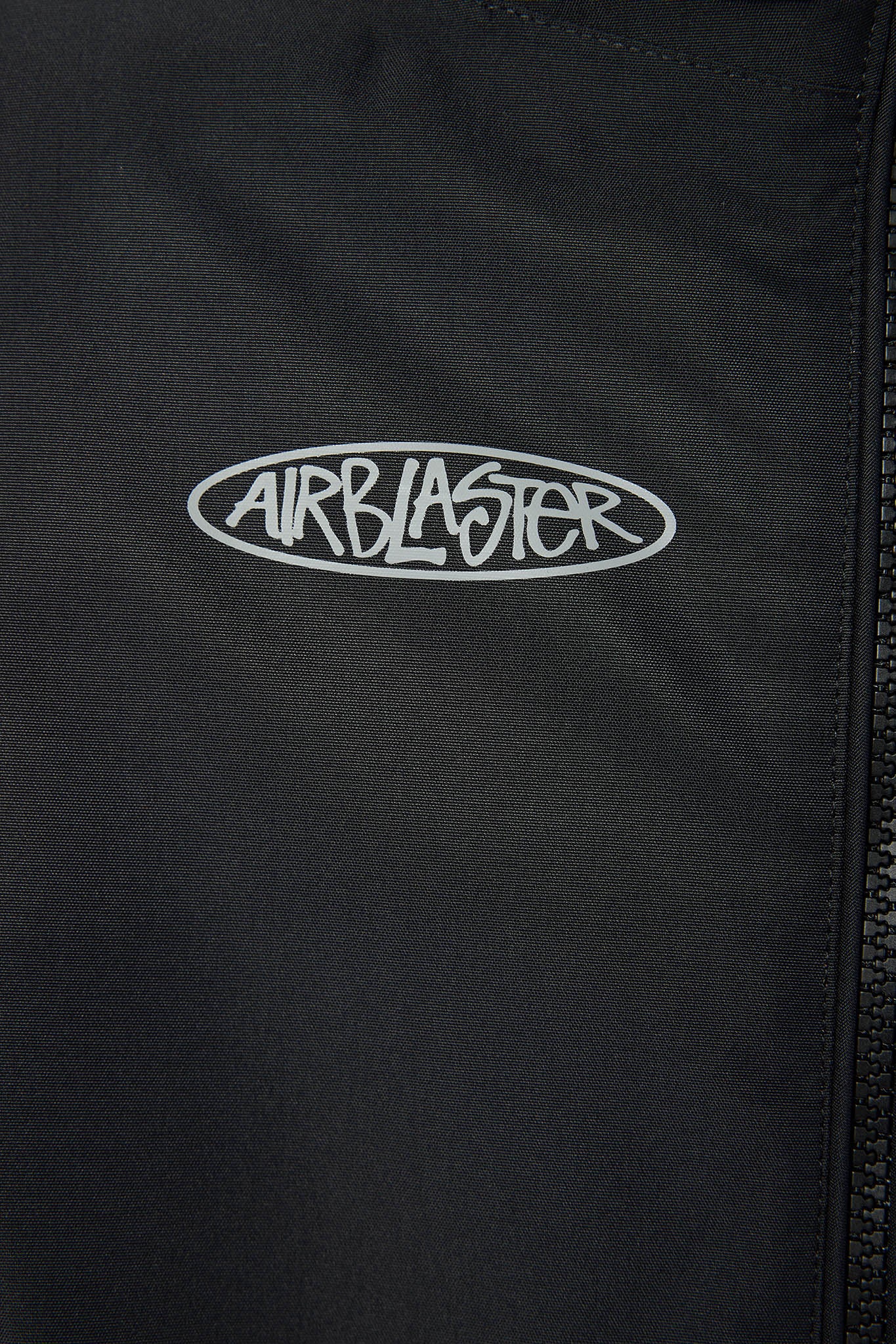 Close-up of a black zippered jacket or windbreaker with a white embroidered oval Airblaster logo on the chest.