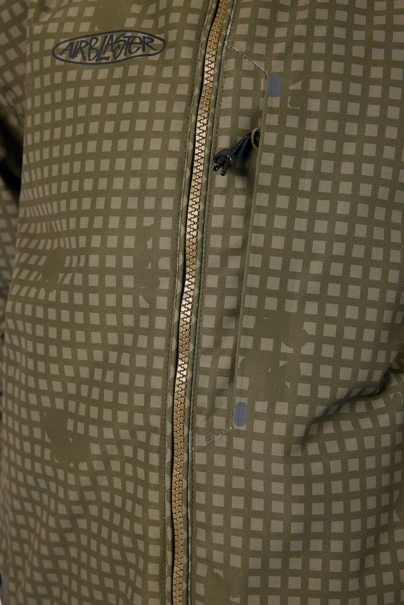 Close-up of a Carblaster jacket featuring a muted olive green and gray grid pattern, a central zipper, and a black Carblaster logo patch on the upper chest.