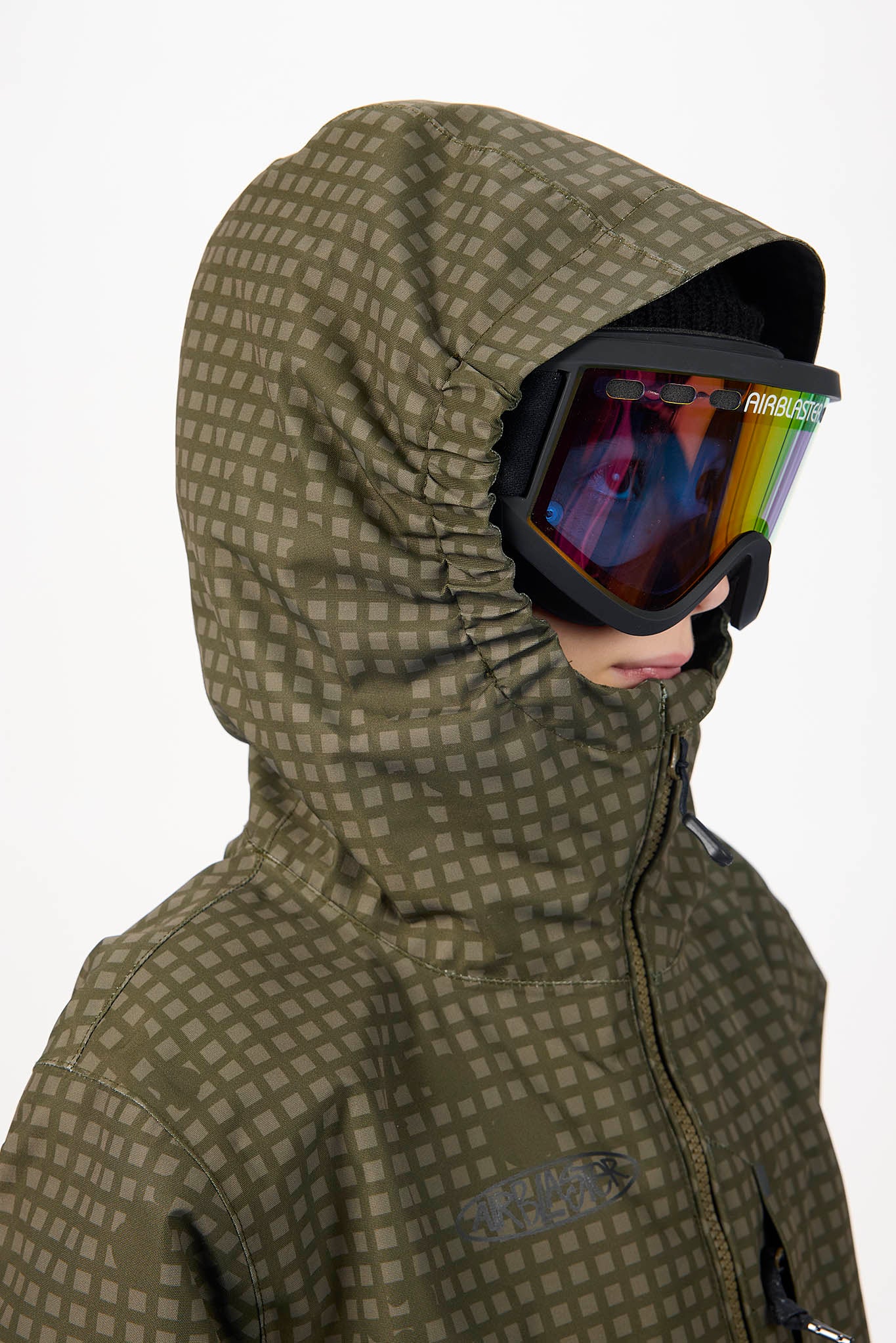 A close-up of a person wearing a hooded ski jacket with a subtle brown and olive green checkered pattern, black goggles, and a visible Patagonia logo on the strap.