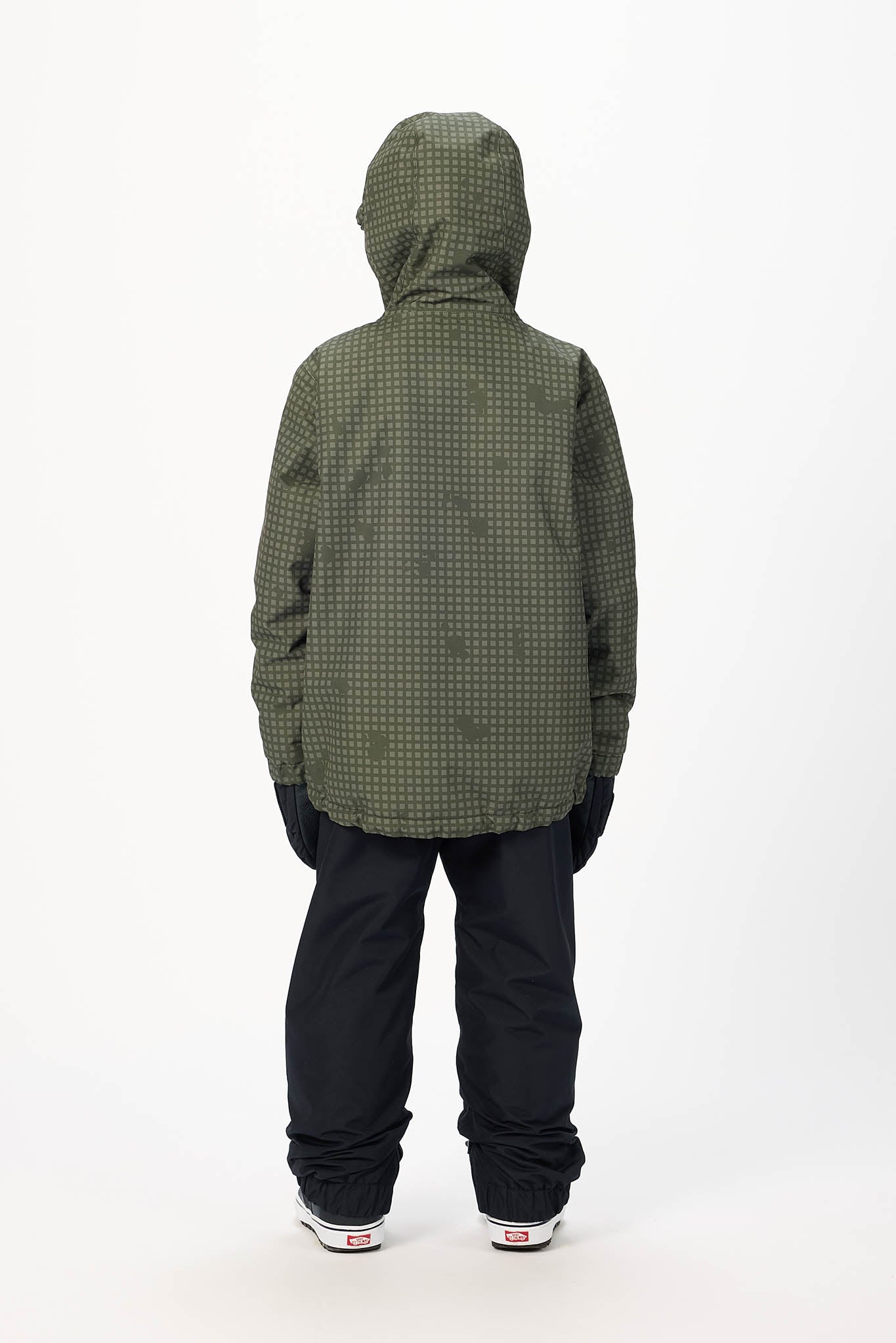 A child viewed from the back wearing an olive green hooded jacket with a subtle tonal pattern, black snow pants, and white sneakers, standing against a plain white studio background.