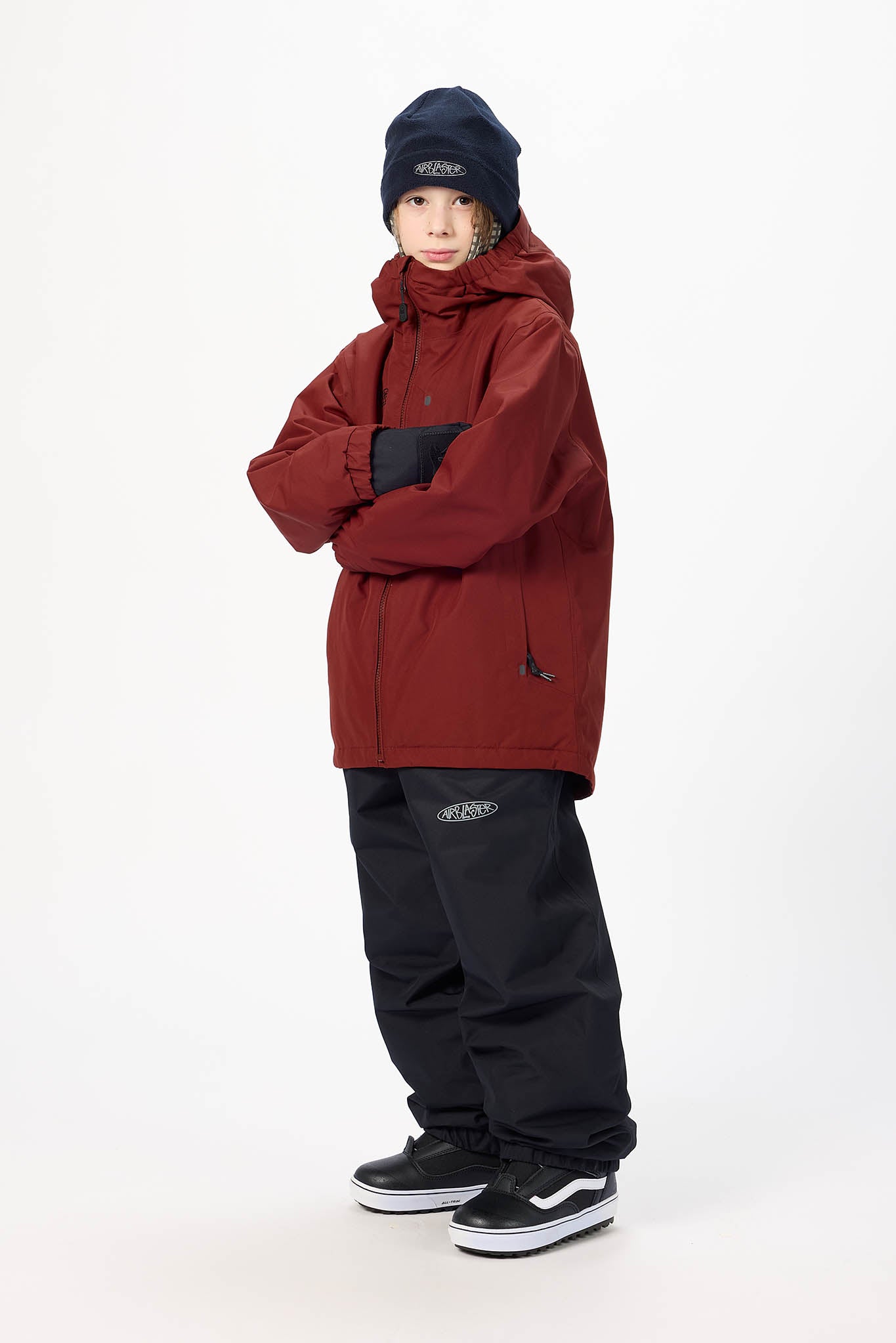 A child model wearing a dark red hooded snowboard jacket, black snow pants, a black beanie, and black skate shoes, standing against a plain white studio background.