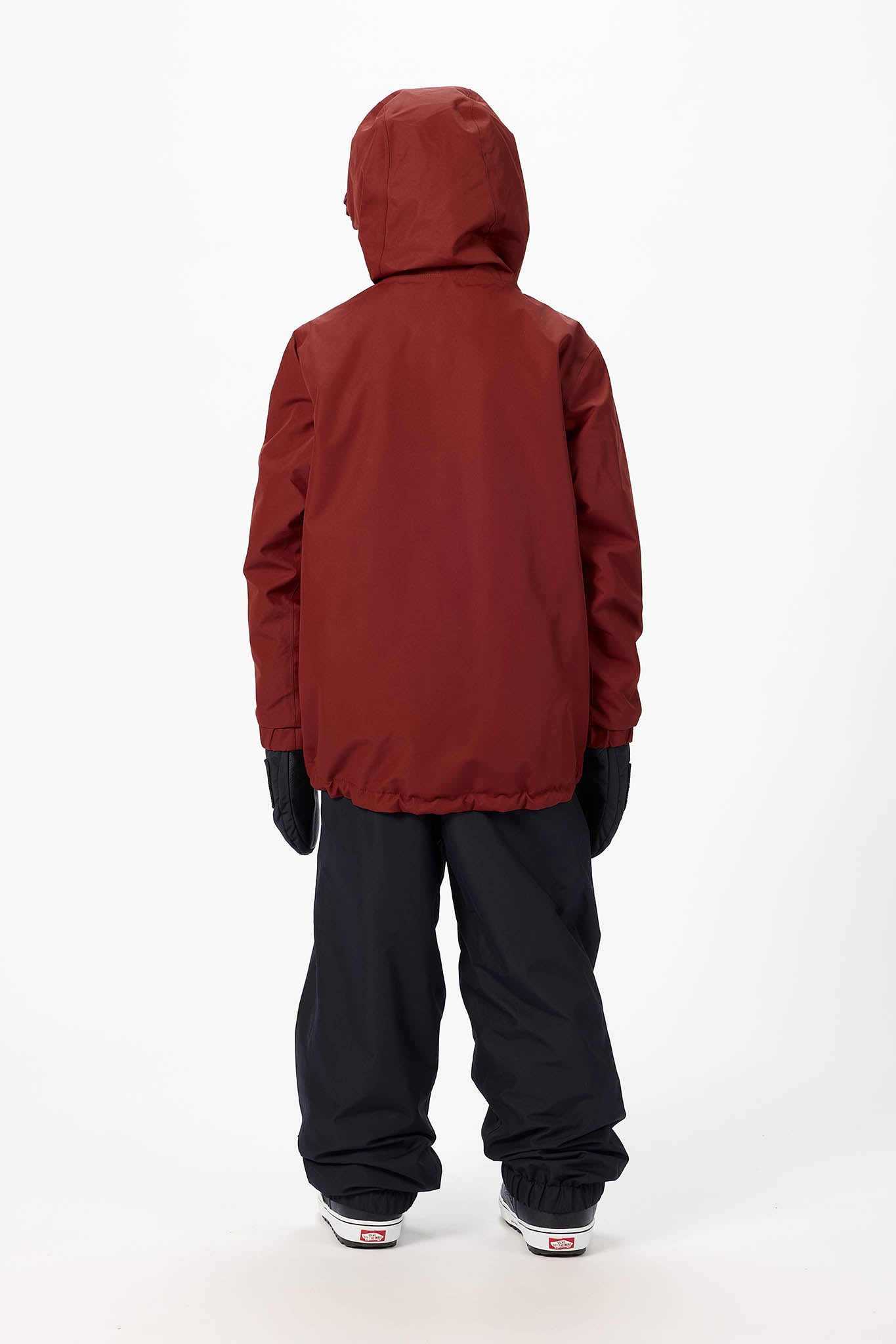 A child shown from the back wearing a dark red hooded jacket, black snow pants, black gloves, and sneakers, standing against a plain white studio background.