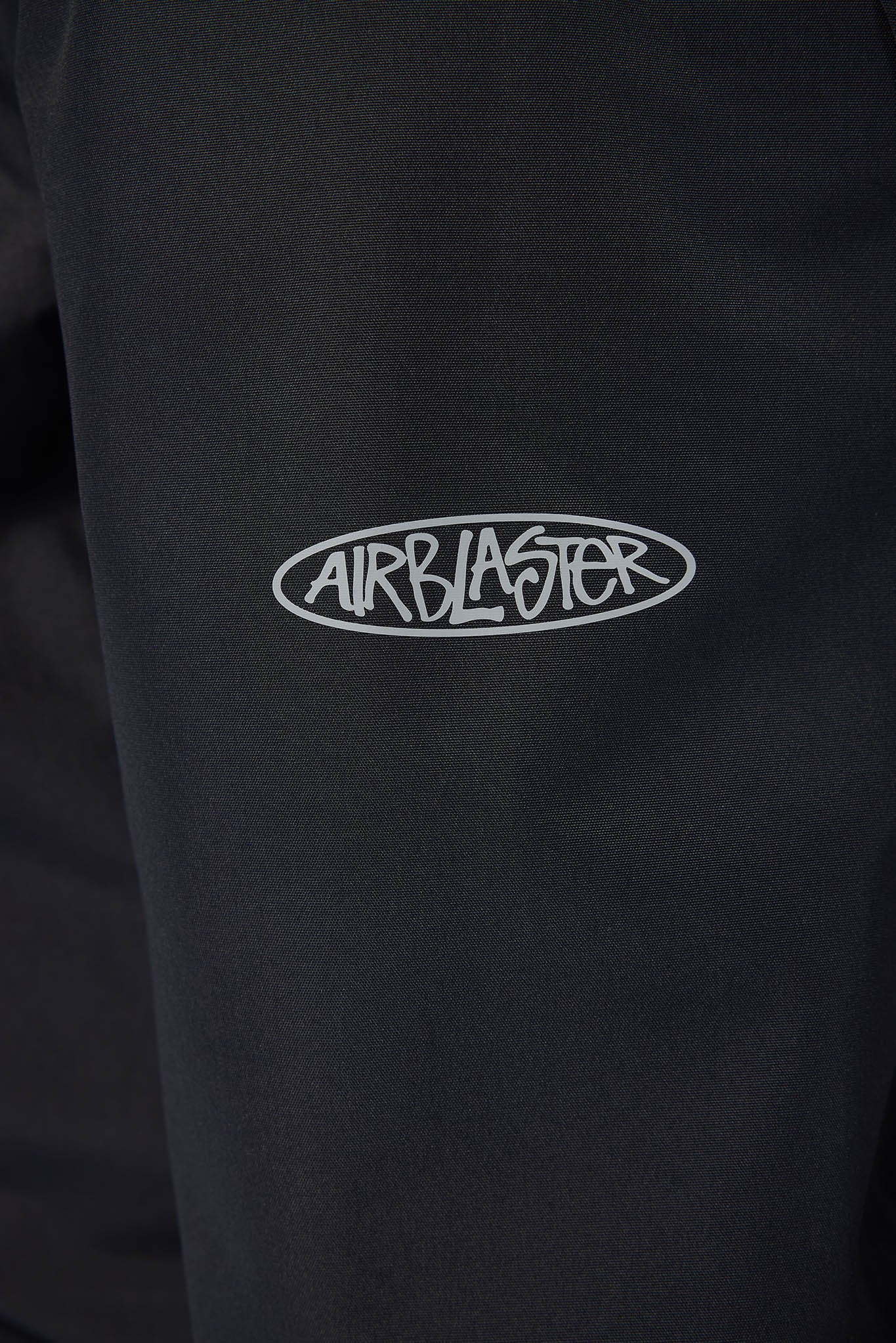 Close-up of a black garment featuring a white embroidered oval logo with the brand name 'AIRBLASTER' across the chest.