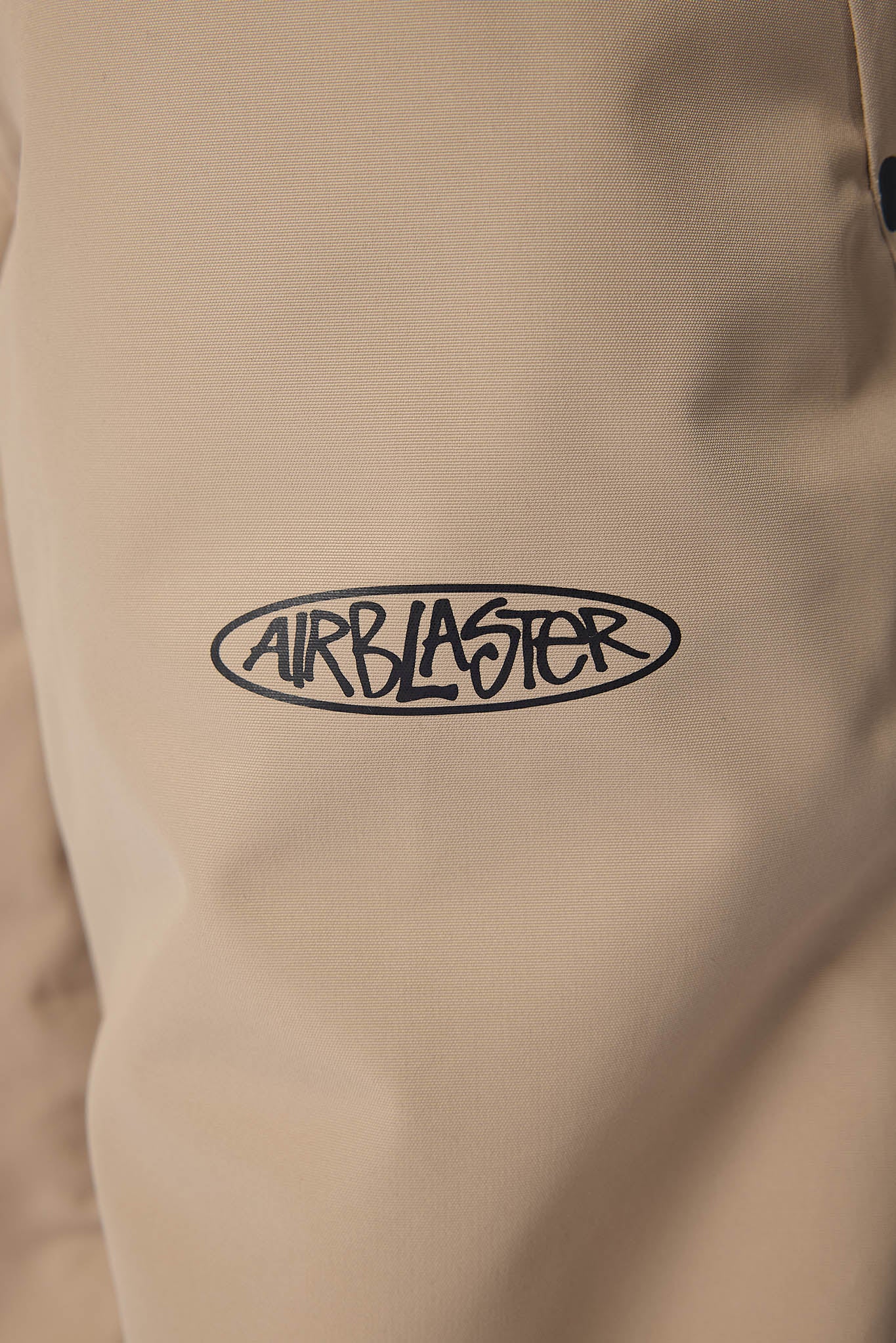 Close-up of a light beige or cream-colored garment with a black oval 'AIRBLASTER' logo printed across the center.