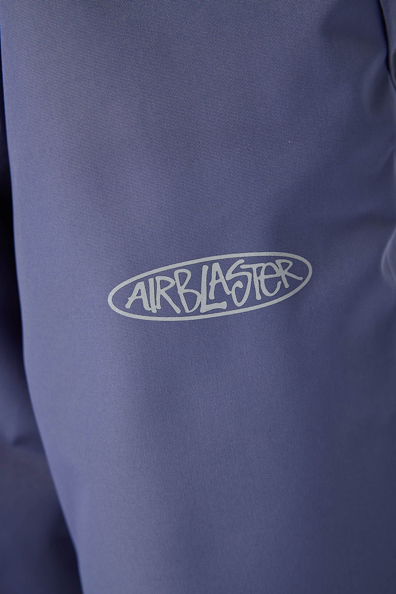Close-up of a dusty blue or periwinkle jacket with a white outlined 'AIRBLASTER' logo on the chest.