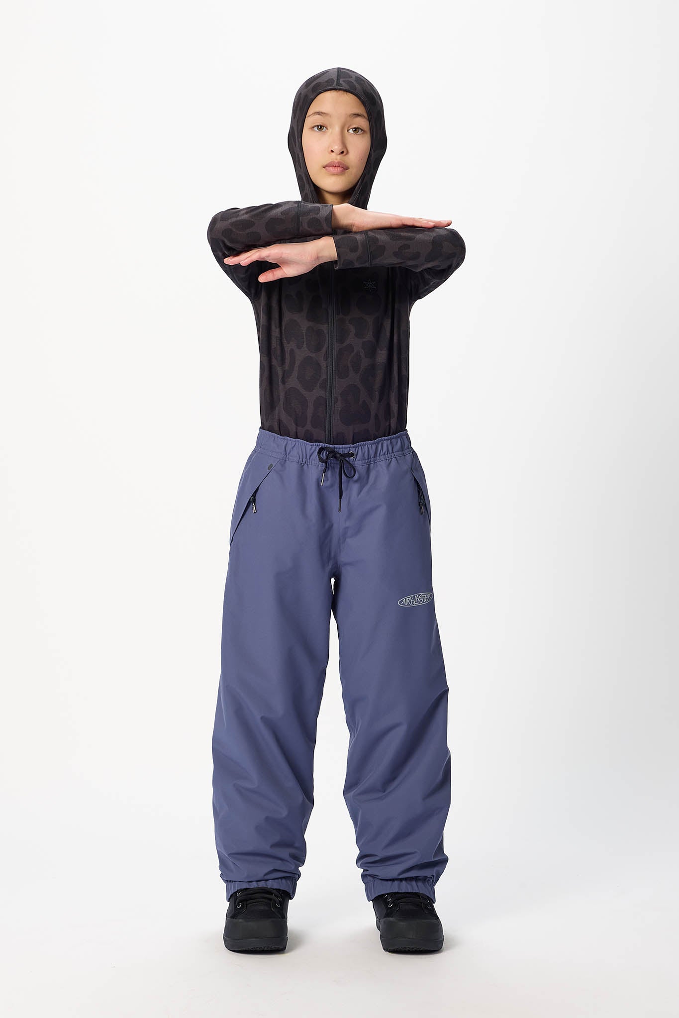 A child model wearing a black patterned long-sleeve top and slate blue drawstring pants, standing against a light gray studio background.