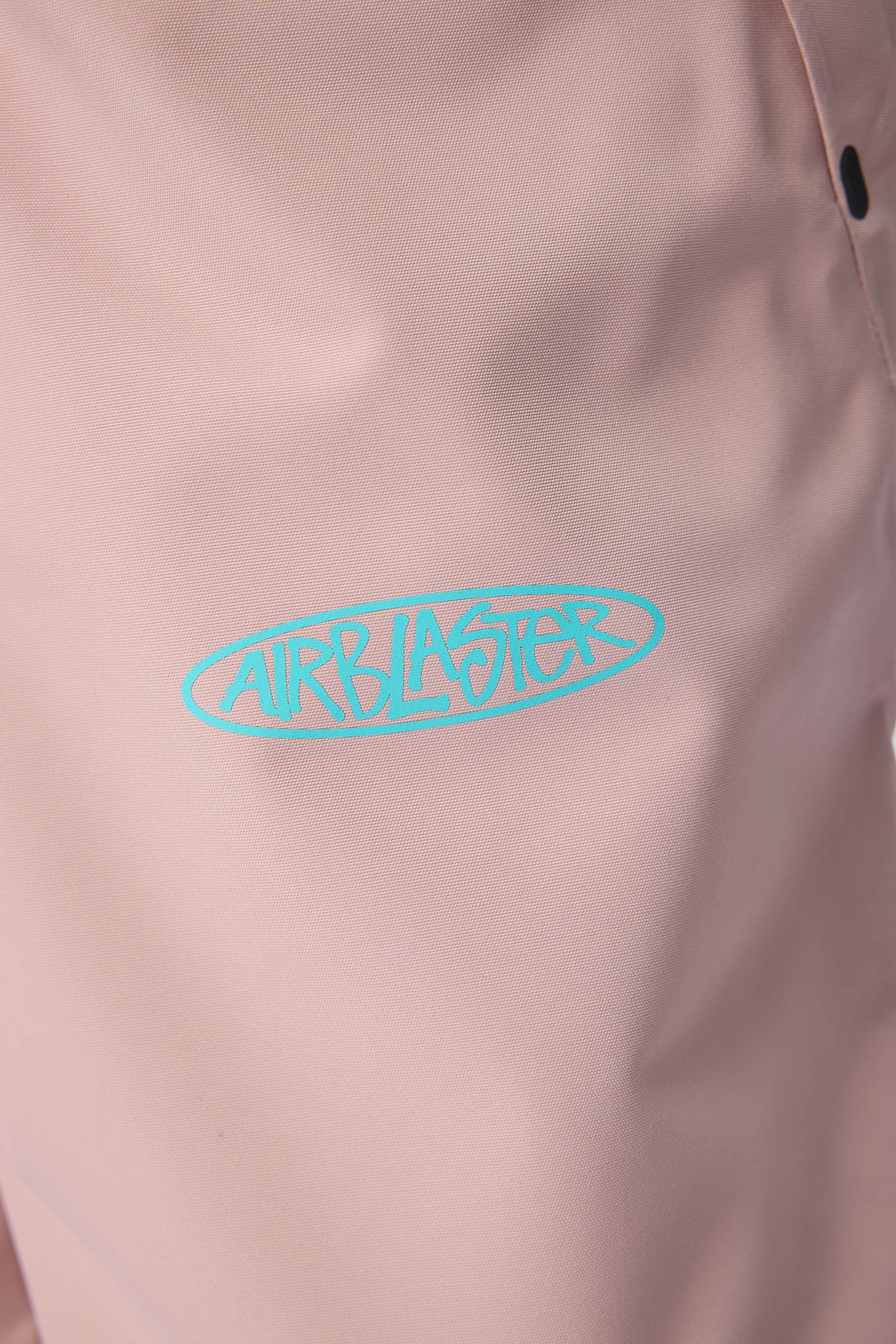 A close-up of a light pink garment featuring a bright turquoise blue 'AIRBLASTER' oval logo printed on the chest.