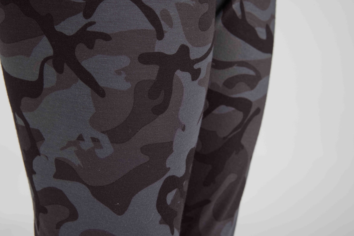 Close-up of leggings with a dark gray and black camouflage pattern, shown on a model against a light gray background.