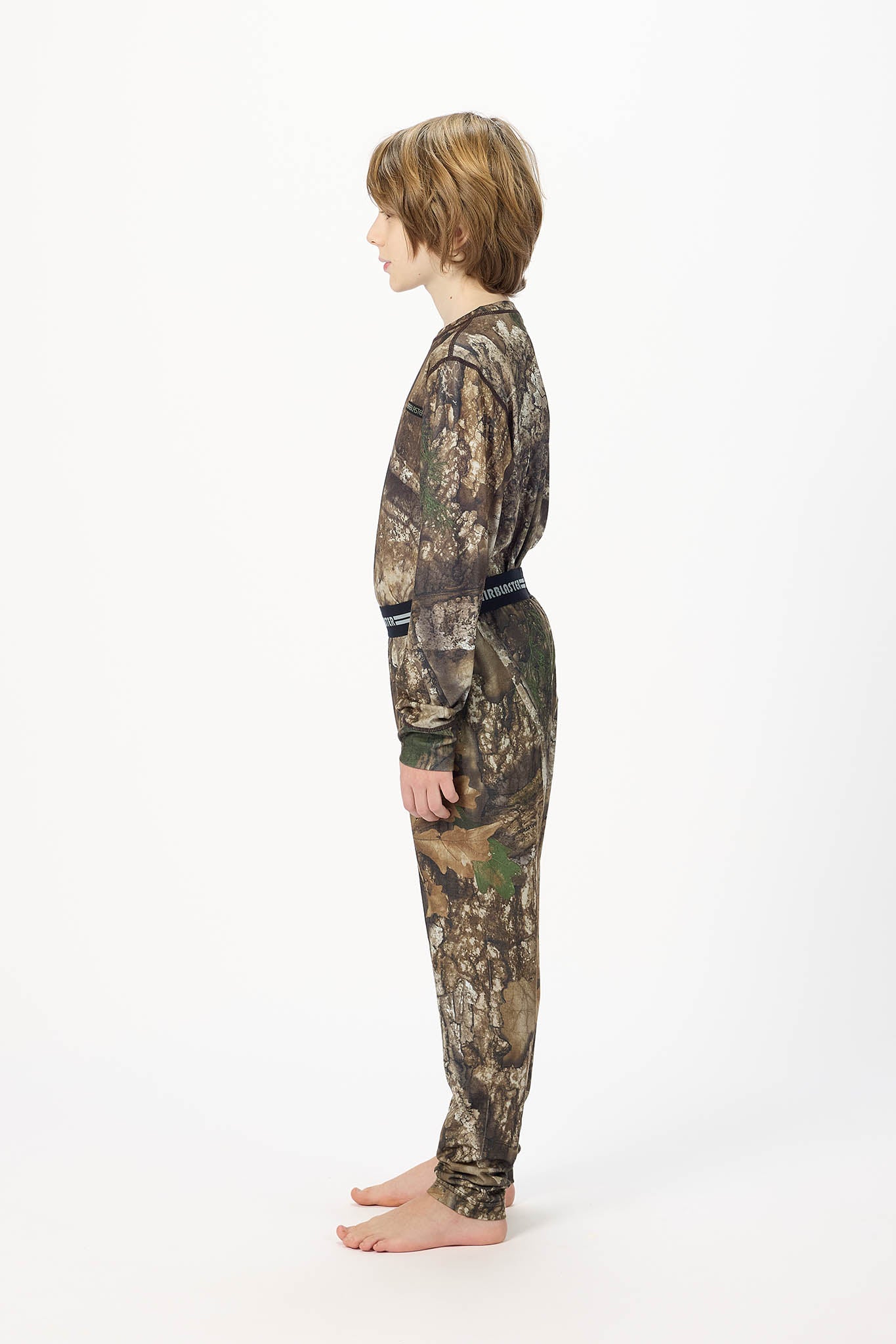 Youth model wearing RealTree Camouflage base layer bottoms,standing sideways.   