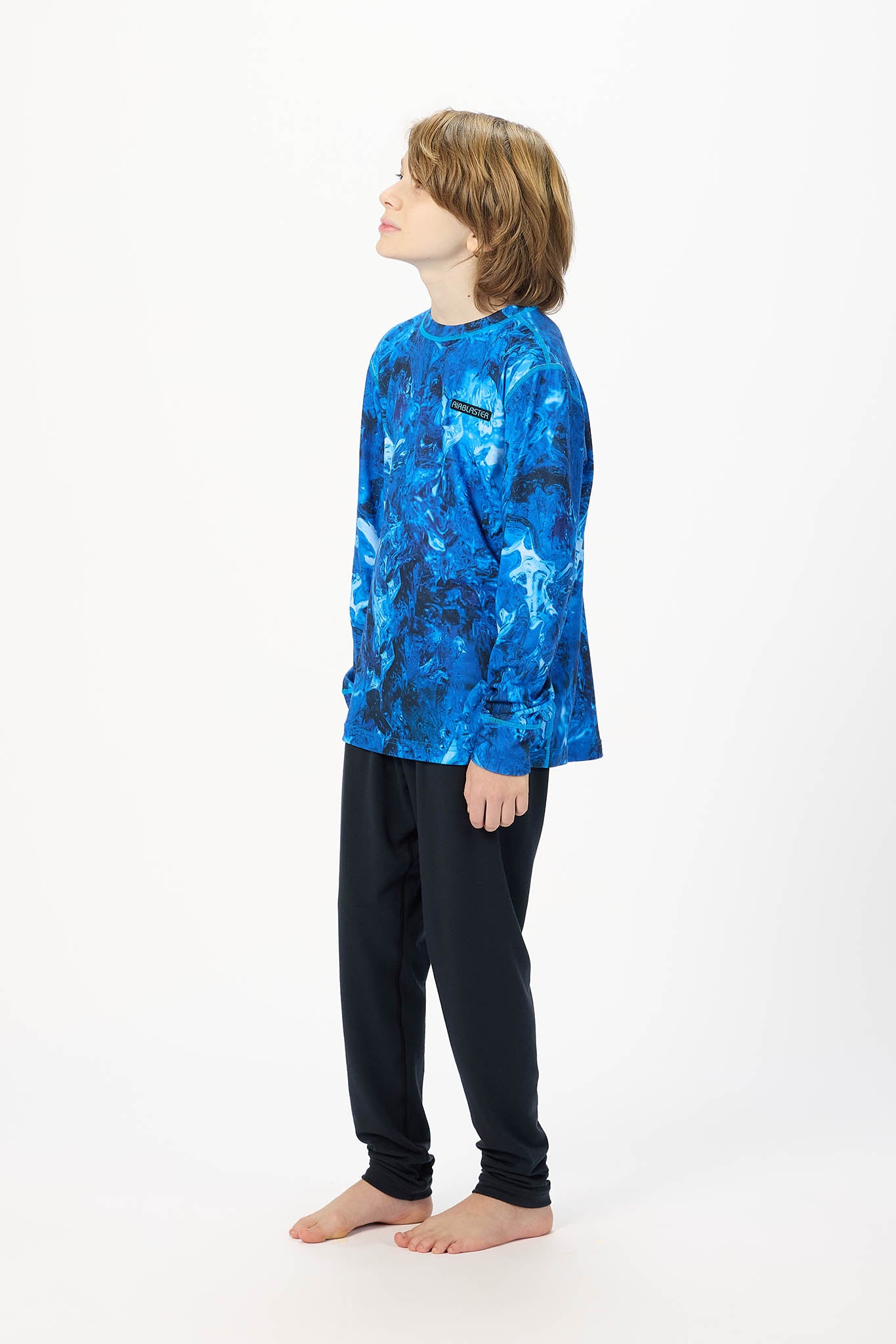 A child model shown in profile wearing a long-sleeve crewneck sweatshirt with a blue and black abstract pattern, paired with black pants, against a plain white studio background.