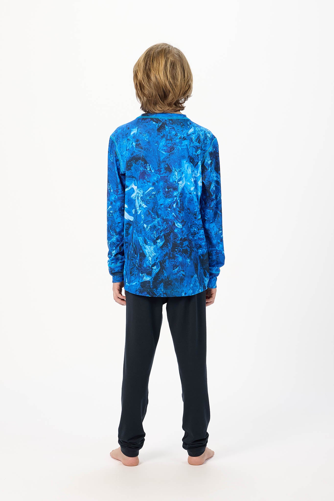 A child standing with their back to the camera, wearing a vibrant blue long-sleeve shirt with an abstract marbled pattern and dark navy pants, against a plain white background.