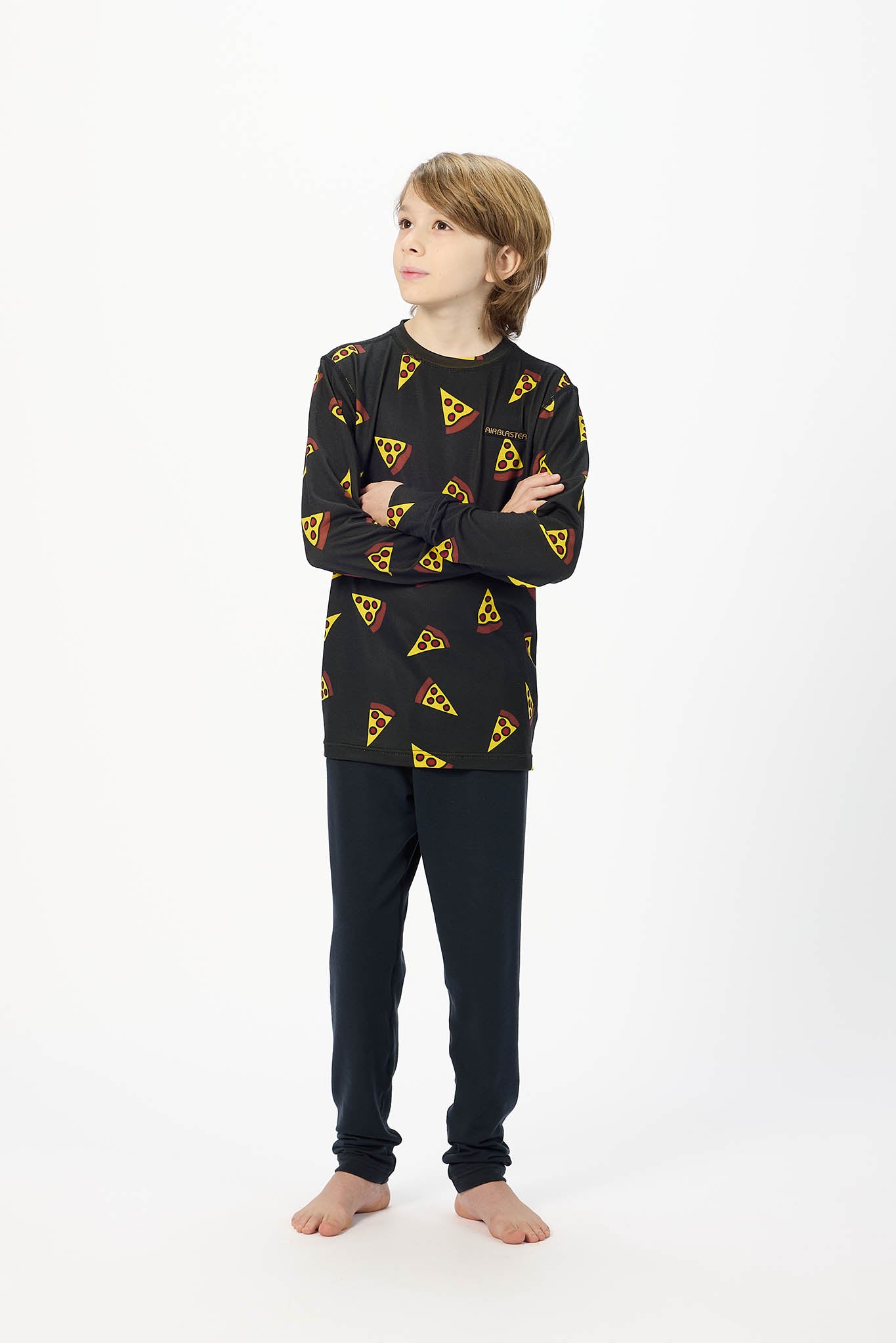 A child model wearing a black long-sleeve pajama top with a yellow and red pizza slice pattern, paired with dark navy pants, standing against a plain white studio background.