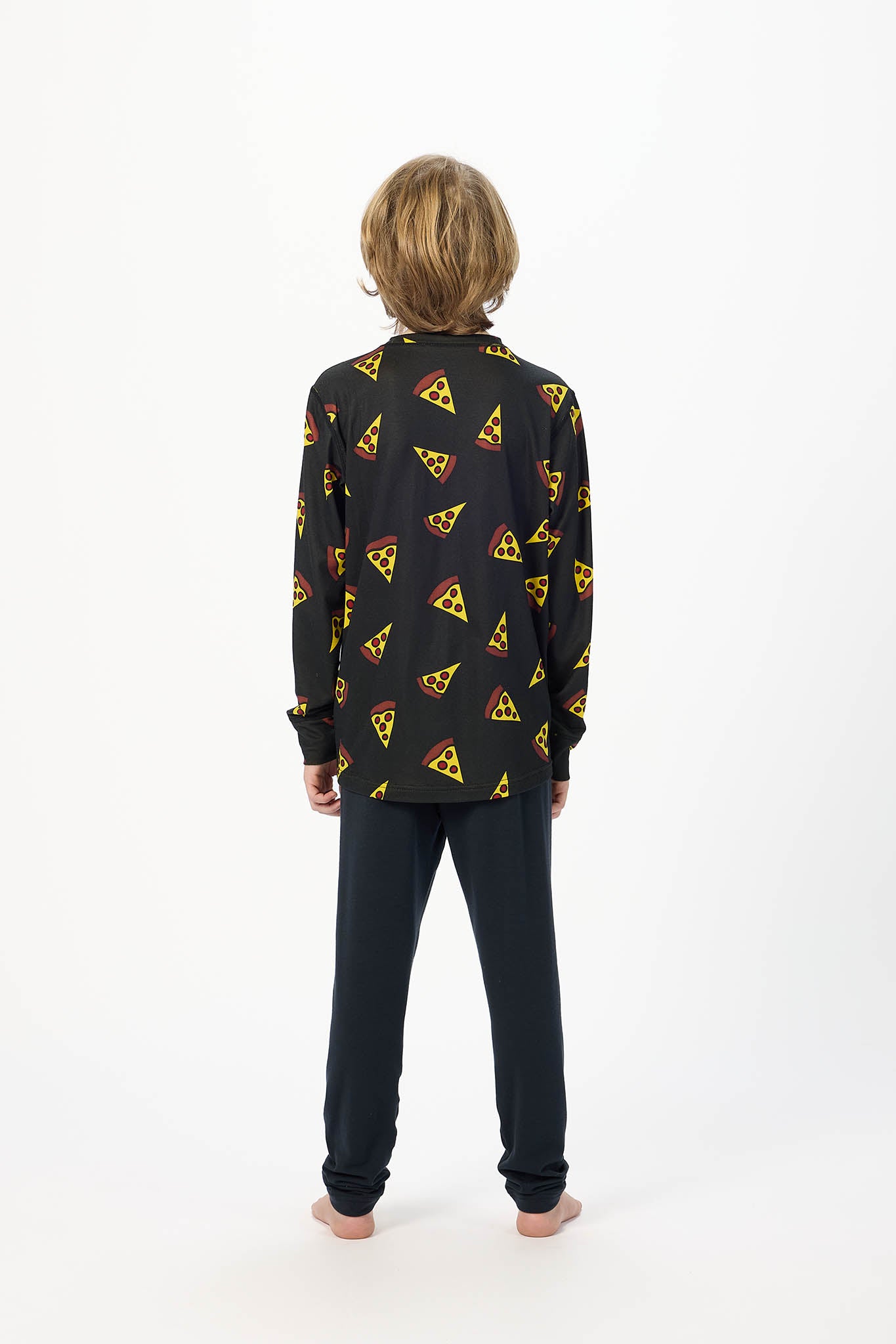 A child standing with their back to the camera, wearing a black long-sleeve button-up shirt with a repeating yellow and red pizza slice pattern, paired with dark pants, against a plain white studio background.