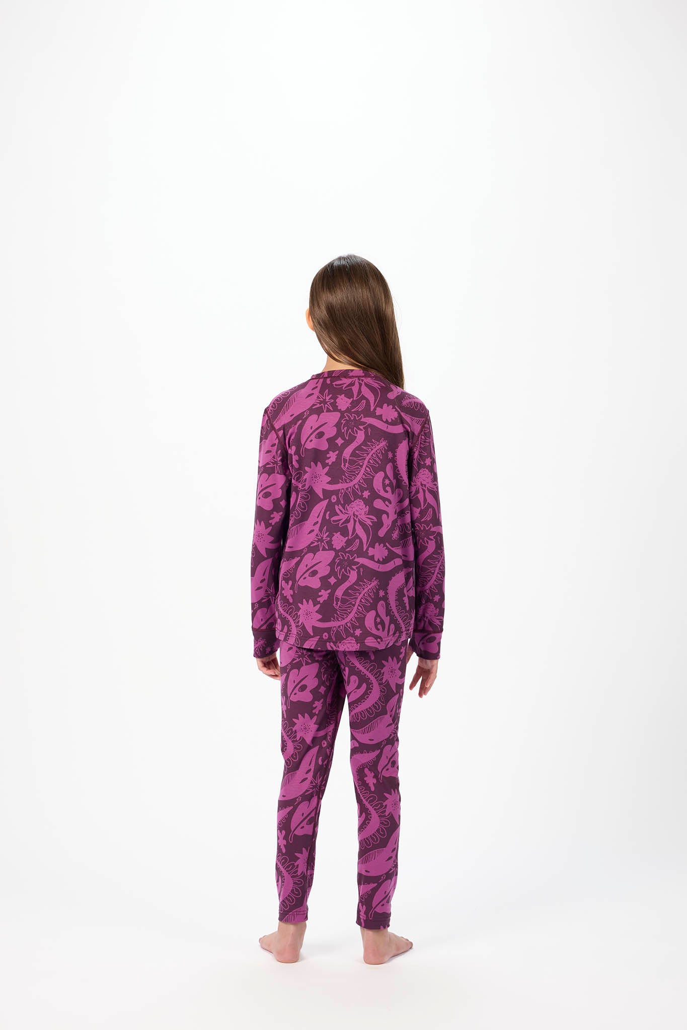 A child standing with their back to the camera, wearing a matching two-piece pajama set with a purple and black abstract pattern, set against a plain white studio background.