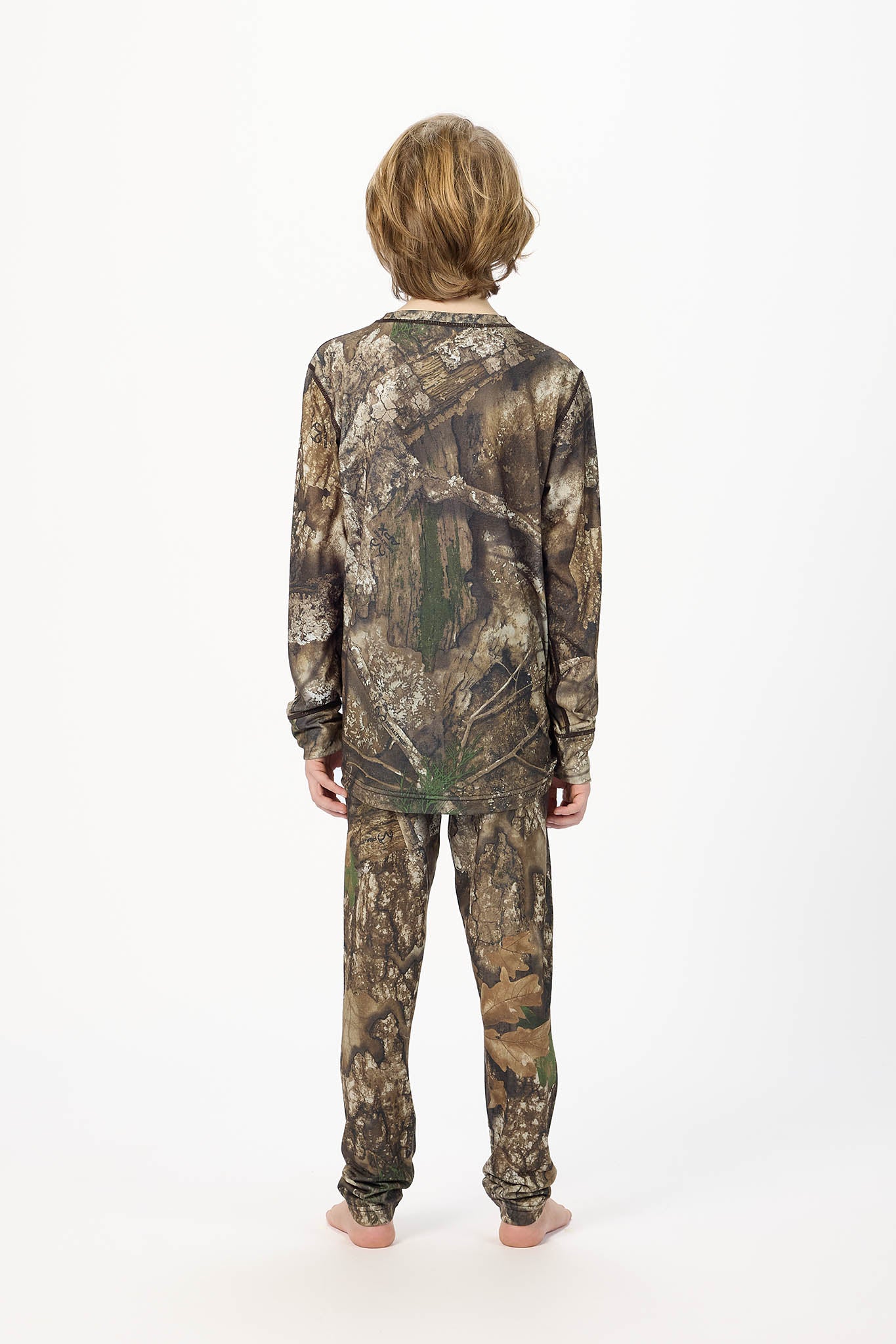 A child standing with their back to the camera, wearing a matching camouflage long-sleeve shirt and pants set against a plain white studio background.