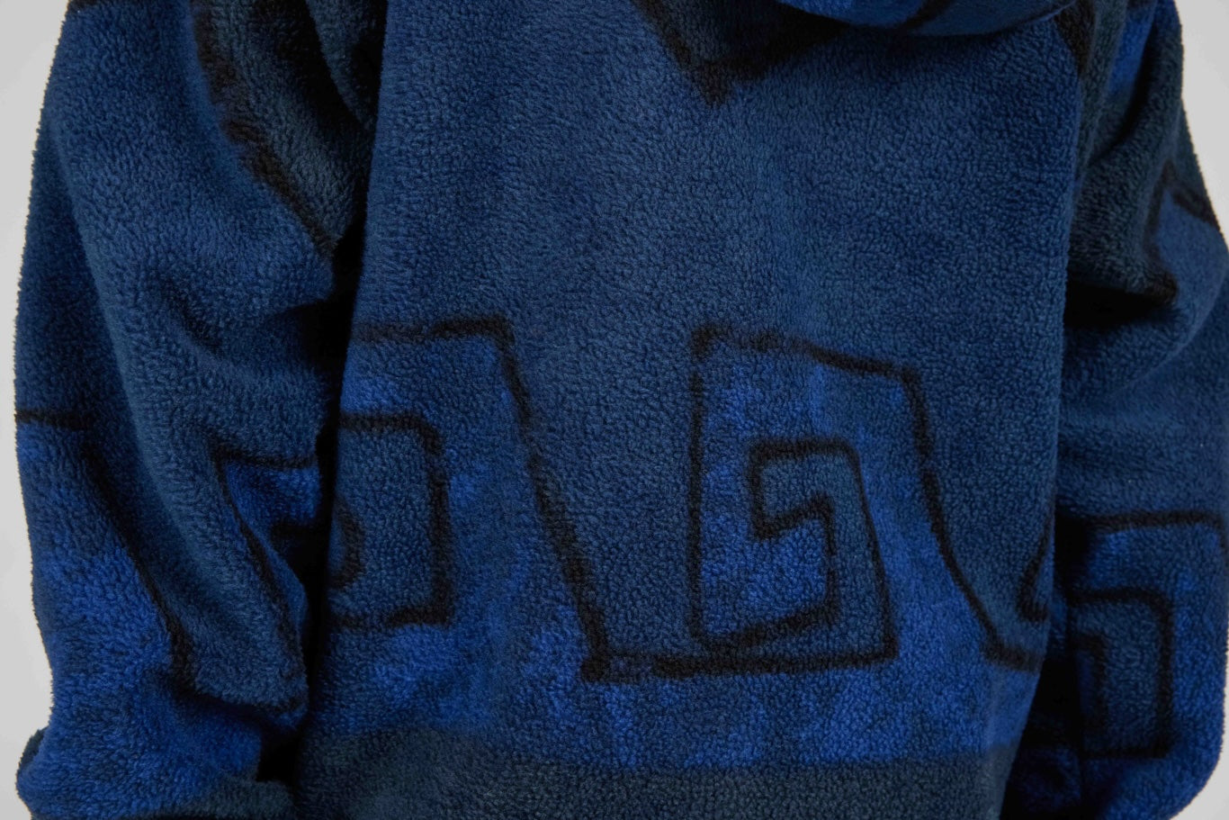 Close-up of a blue textured fleece garment with a dark blue geometric patterned design.
