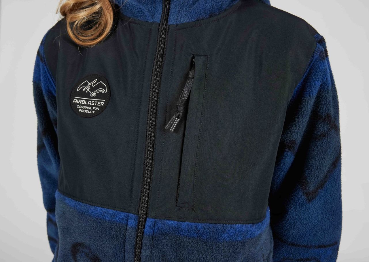 A close-up of a person wearing a color-block fleece jacket. The jacket features a black chest panel, a blue zippered pocket on the chest, and blue fleece sleeves and collar.