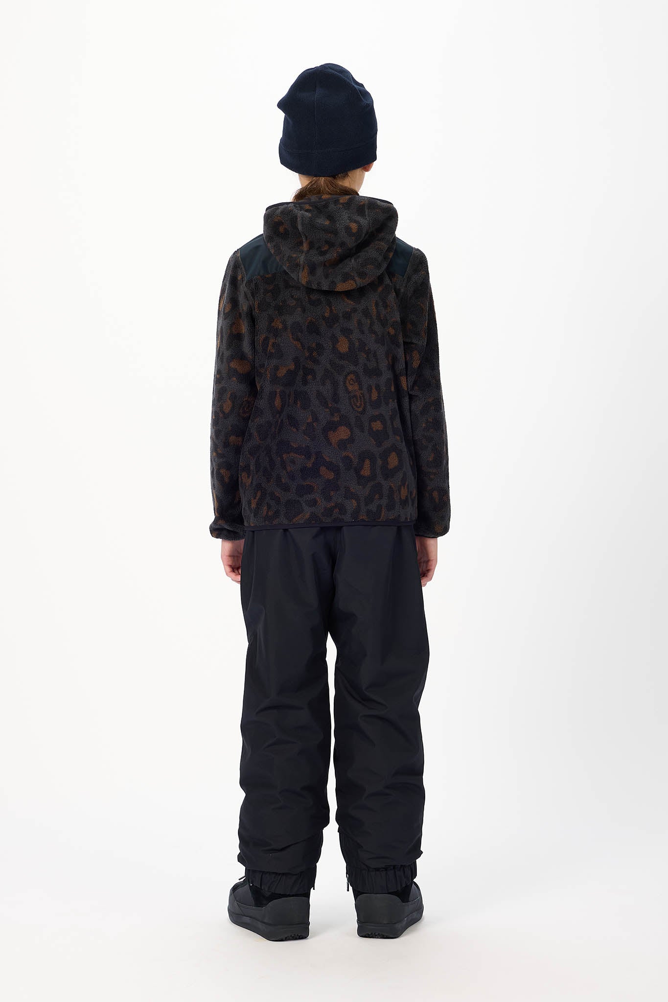 A person shown from the back wearing a dark hooded jacket with an allover leopard-style pattern, black snow pants, and a dark beanie against a plain light gray studio background.