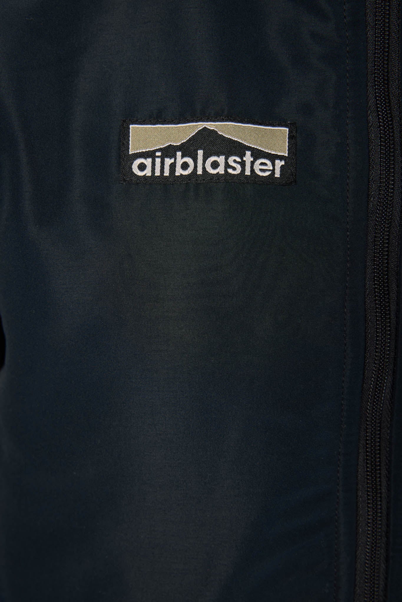 Close-up of a dark navy jacket with a black and beige Airblaster logo patch on the chest.