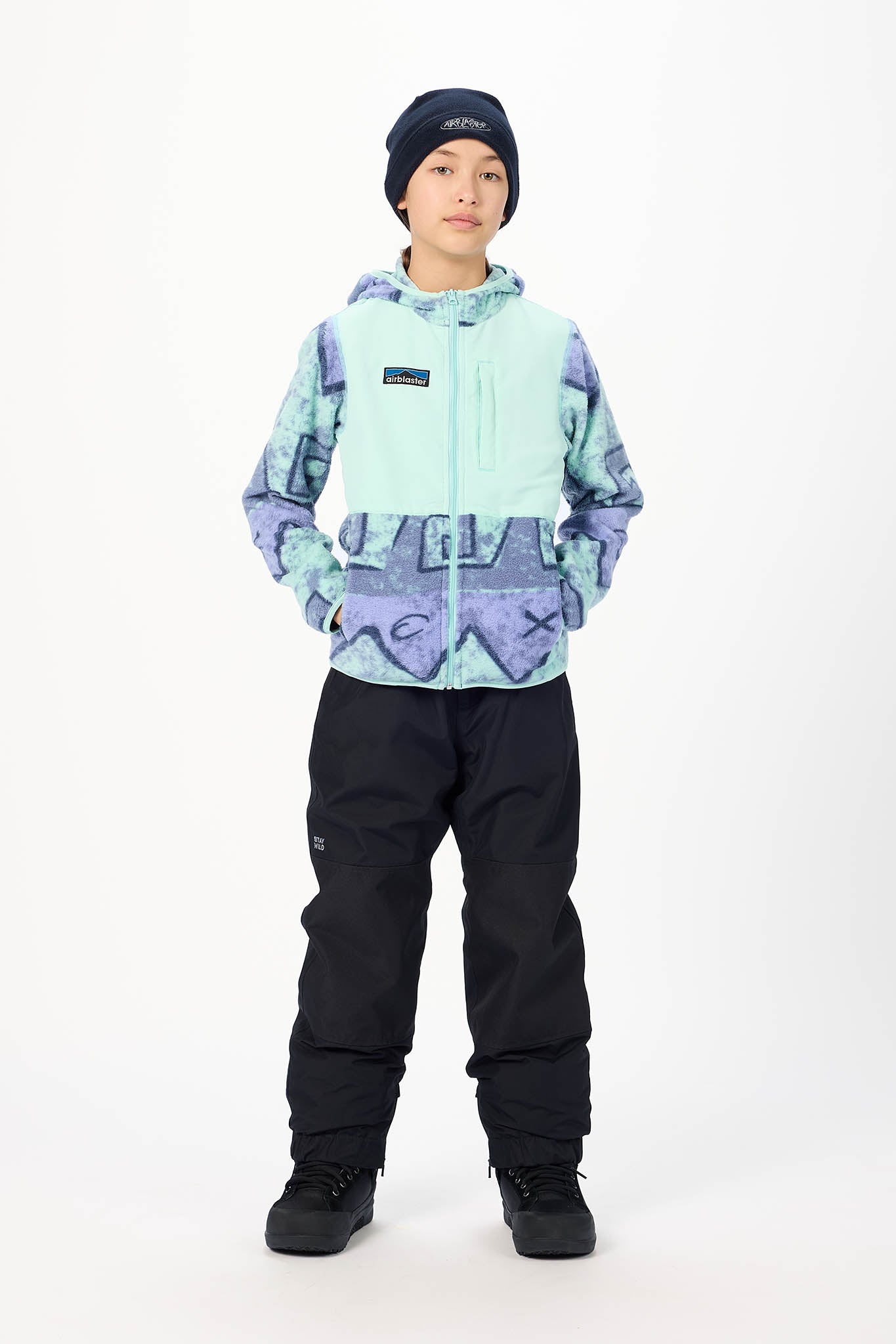 A child model wearing a Patagonia hooded snow jacket with a mint green and purple abstract pattern, black snow pants, and a black beanie, standing against a white studio background.