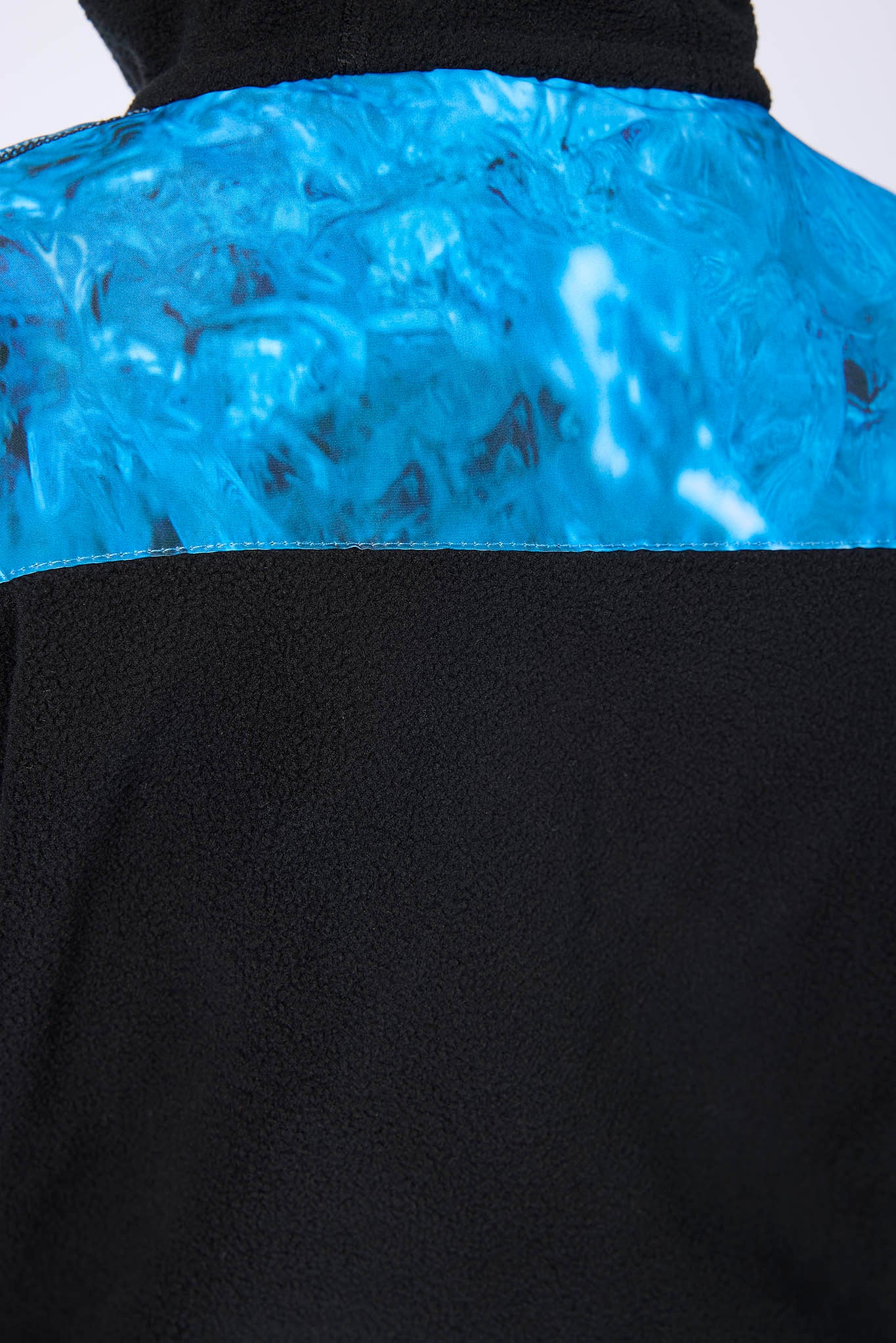 Close-up of the back of a black fleece jacket with a bright blue marbled patterned panel across the upper back.