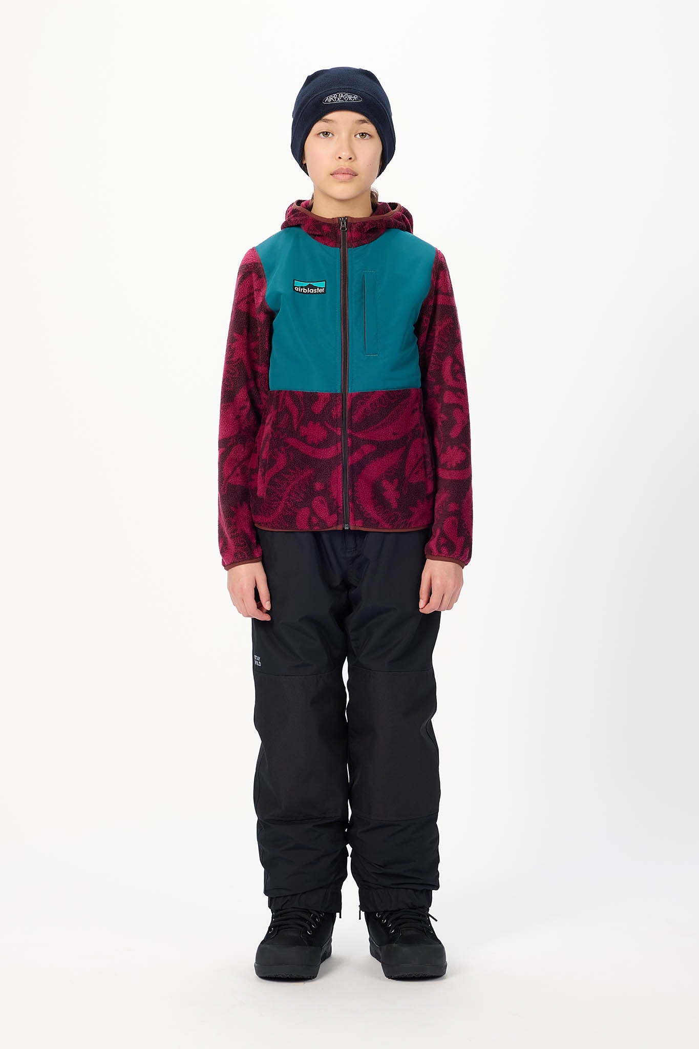 A child model wearing a Patagonia colorblock fleece jacket, black snow pants, a dark navy beanie, and black snow boots, standing against a plain white studio background.