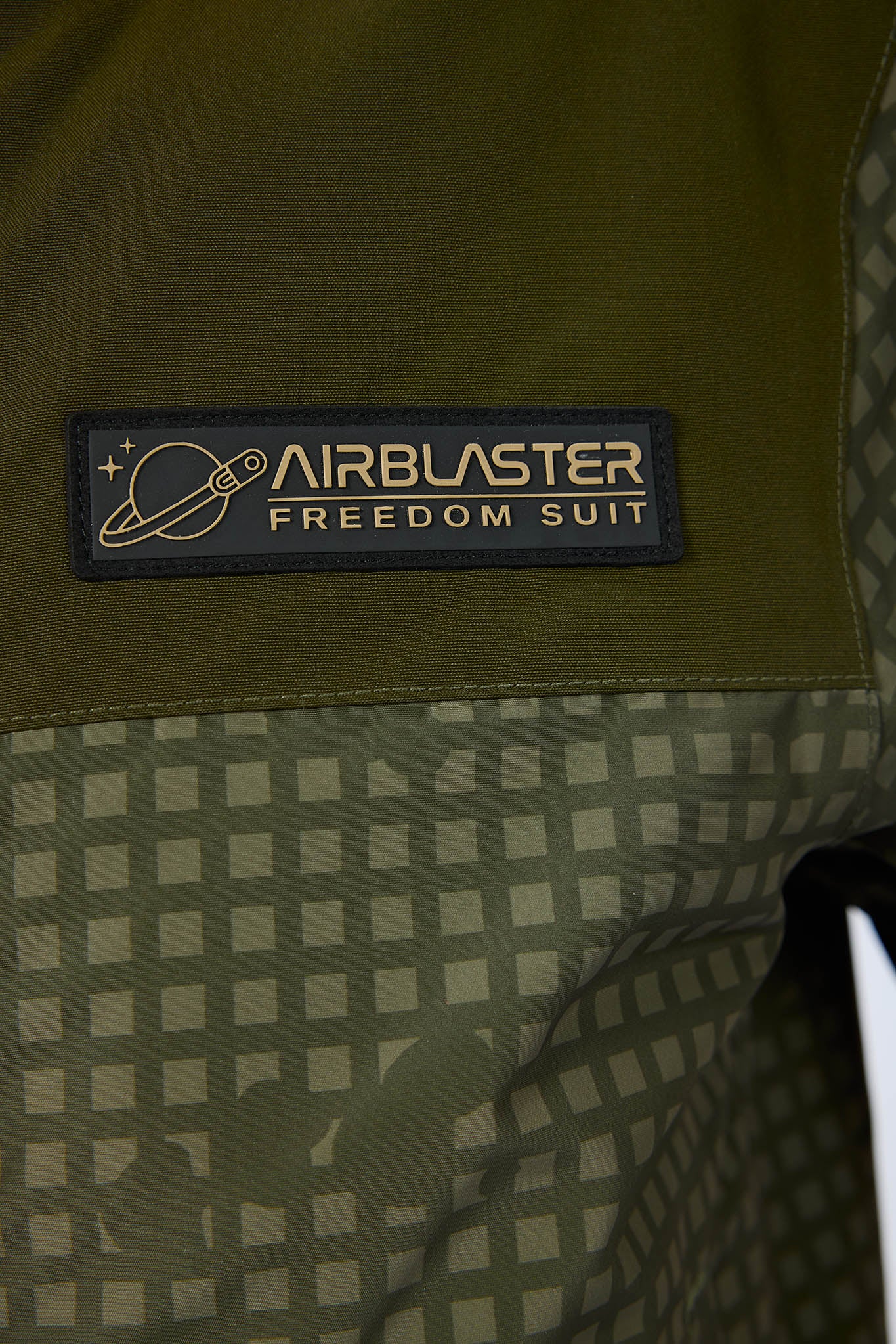 Close-up of a green and beige patterned jacket with a black patch reading 'AIRBLASTER FREEDOM SUIT' on the chest.
